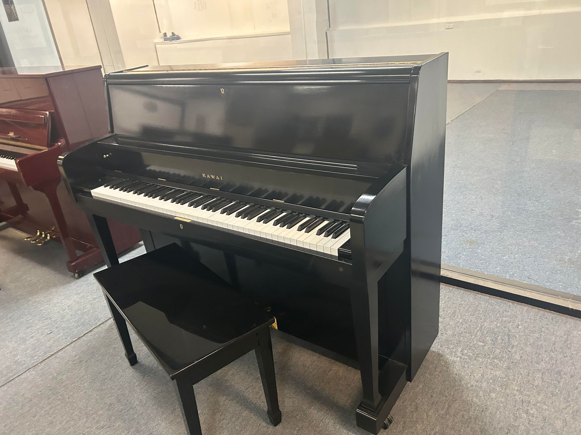 Black upright piano with matching bench in a room with another piano.