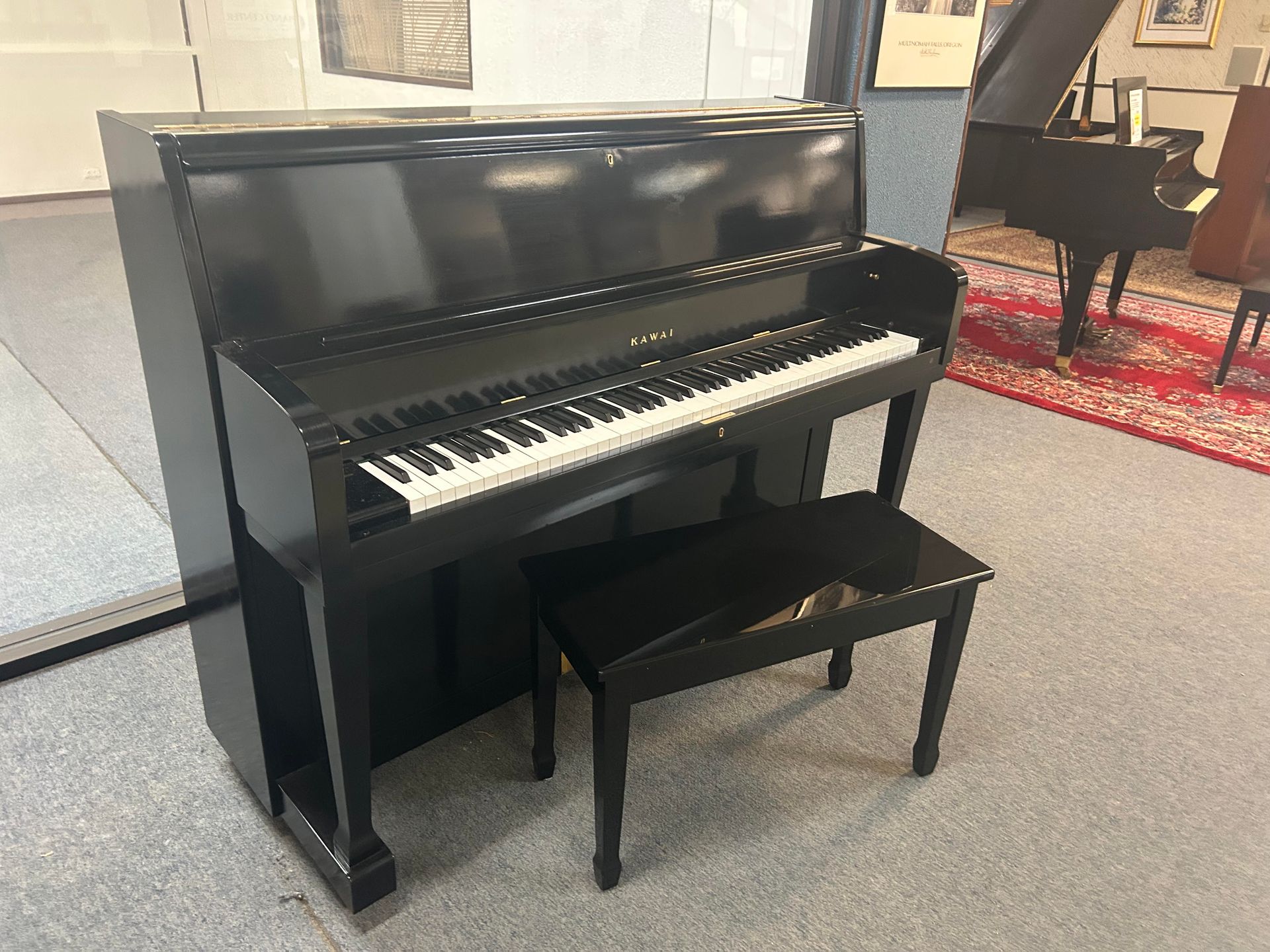 Black upright piano with matching bench in a showroom setting.