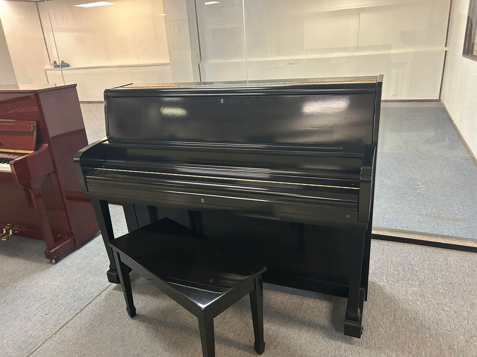 Black upright piano with matching bench in a room with a red piano.