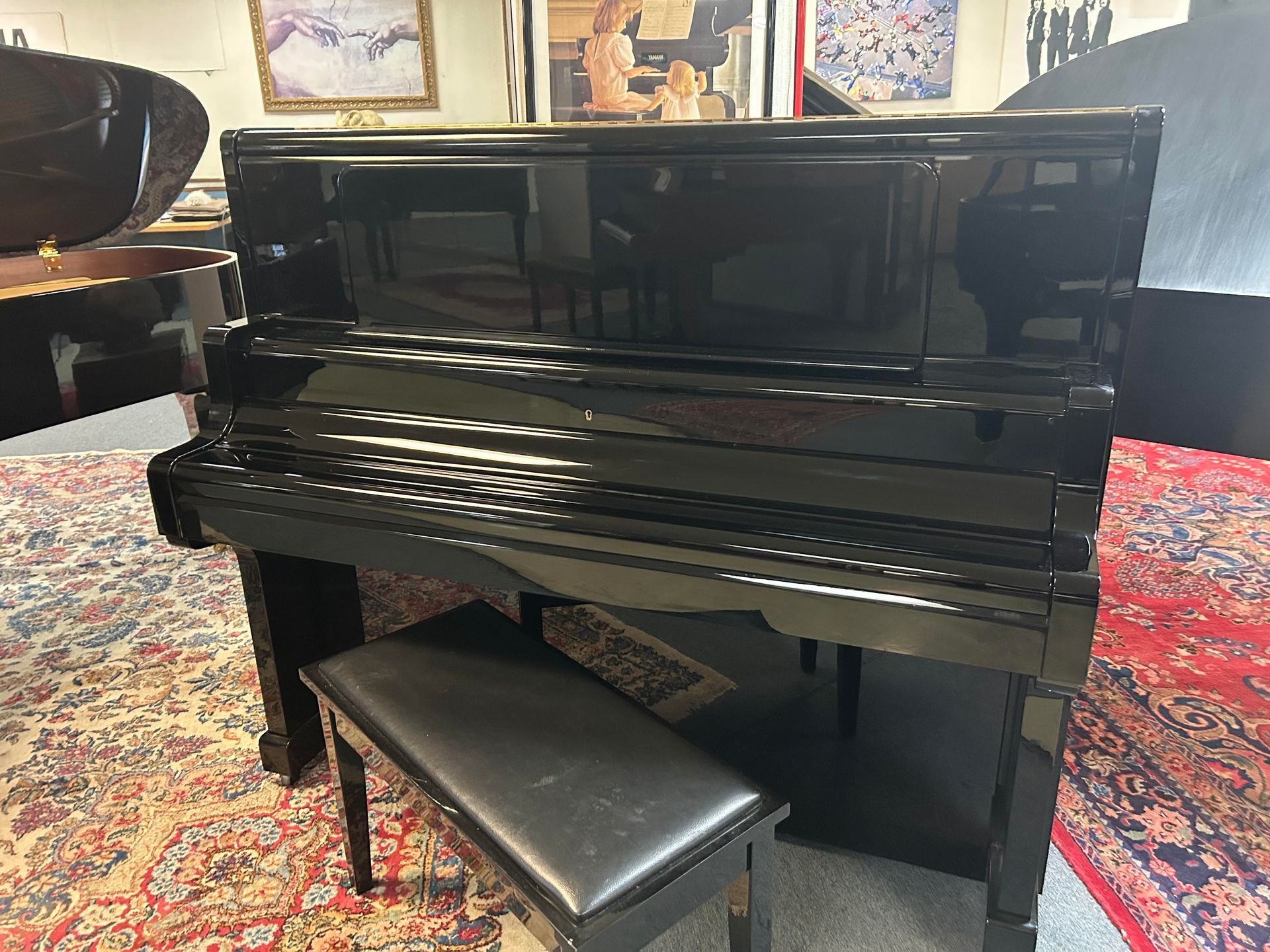 Black upright piano with a matching bench on a patterned rug.