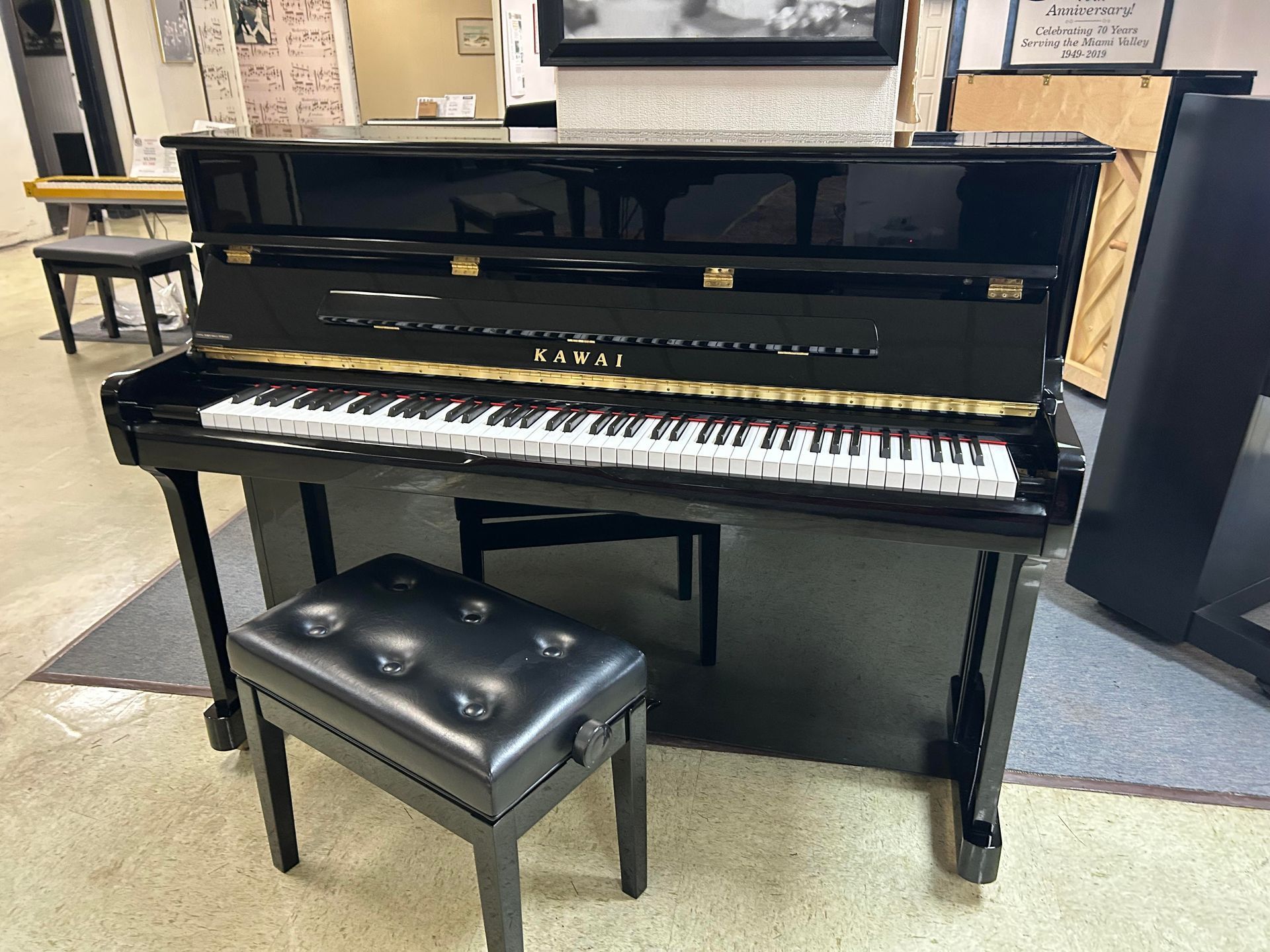 Black Kawai upright piano with bench in a room.