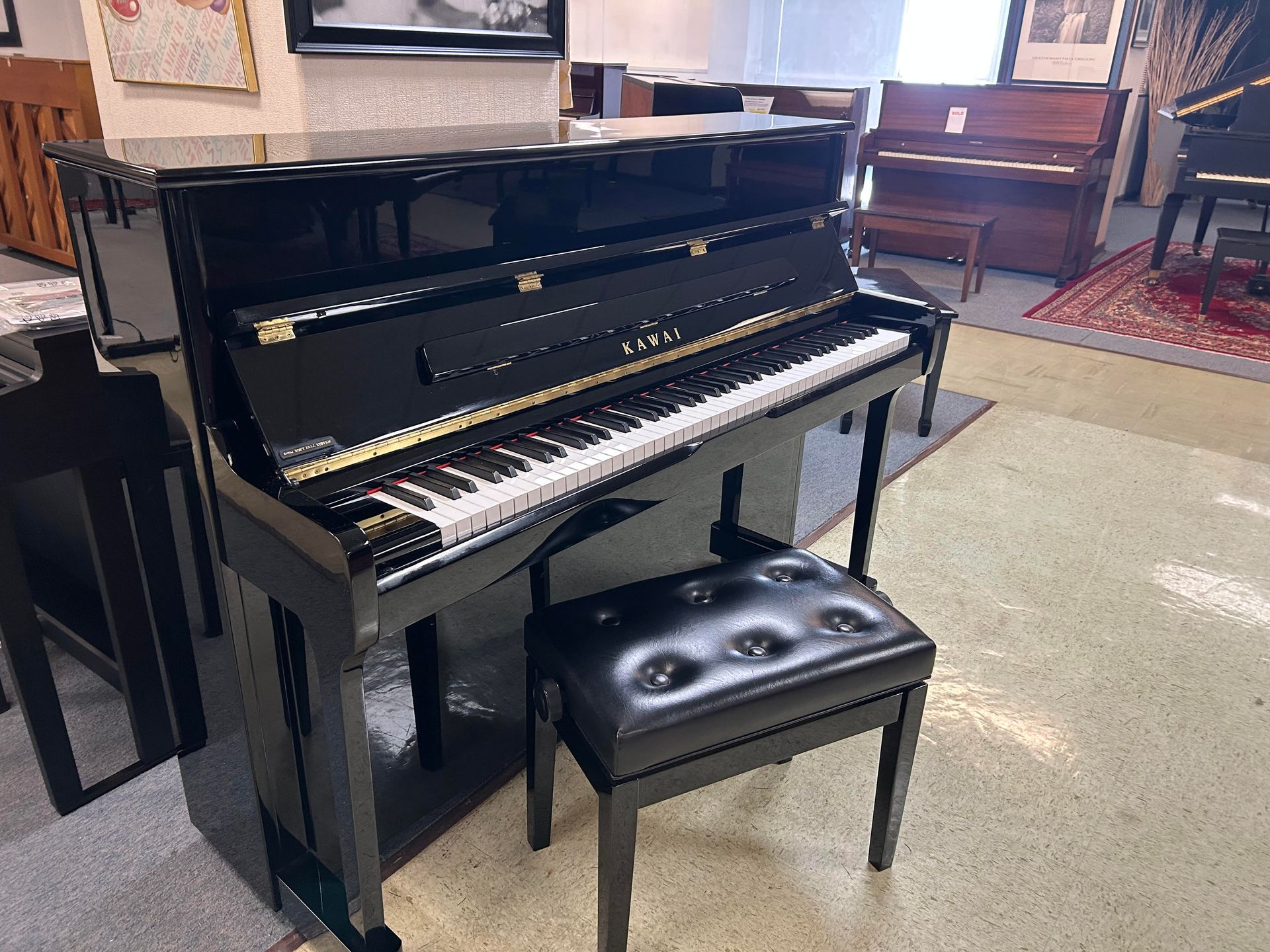Black upright piano with matching stool in a showroom.