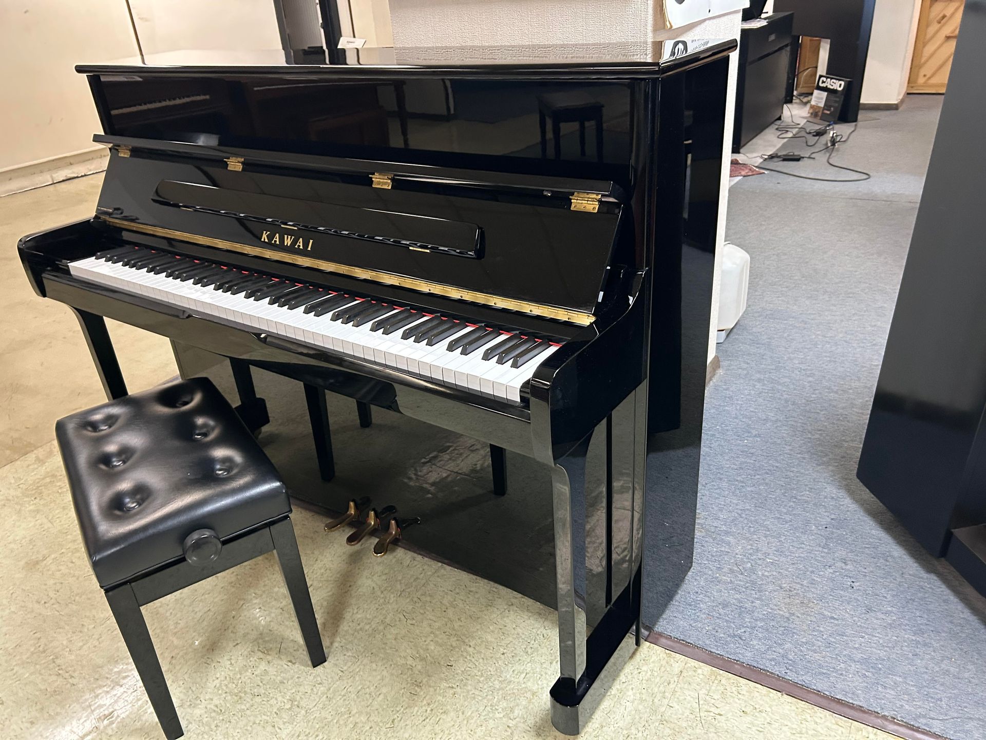 Black upright piano with matching bench in a showroom.