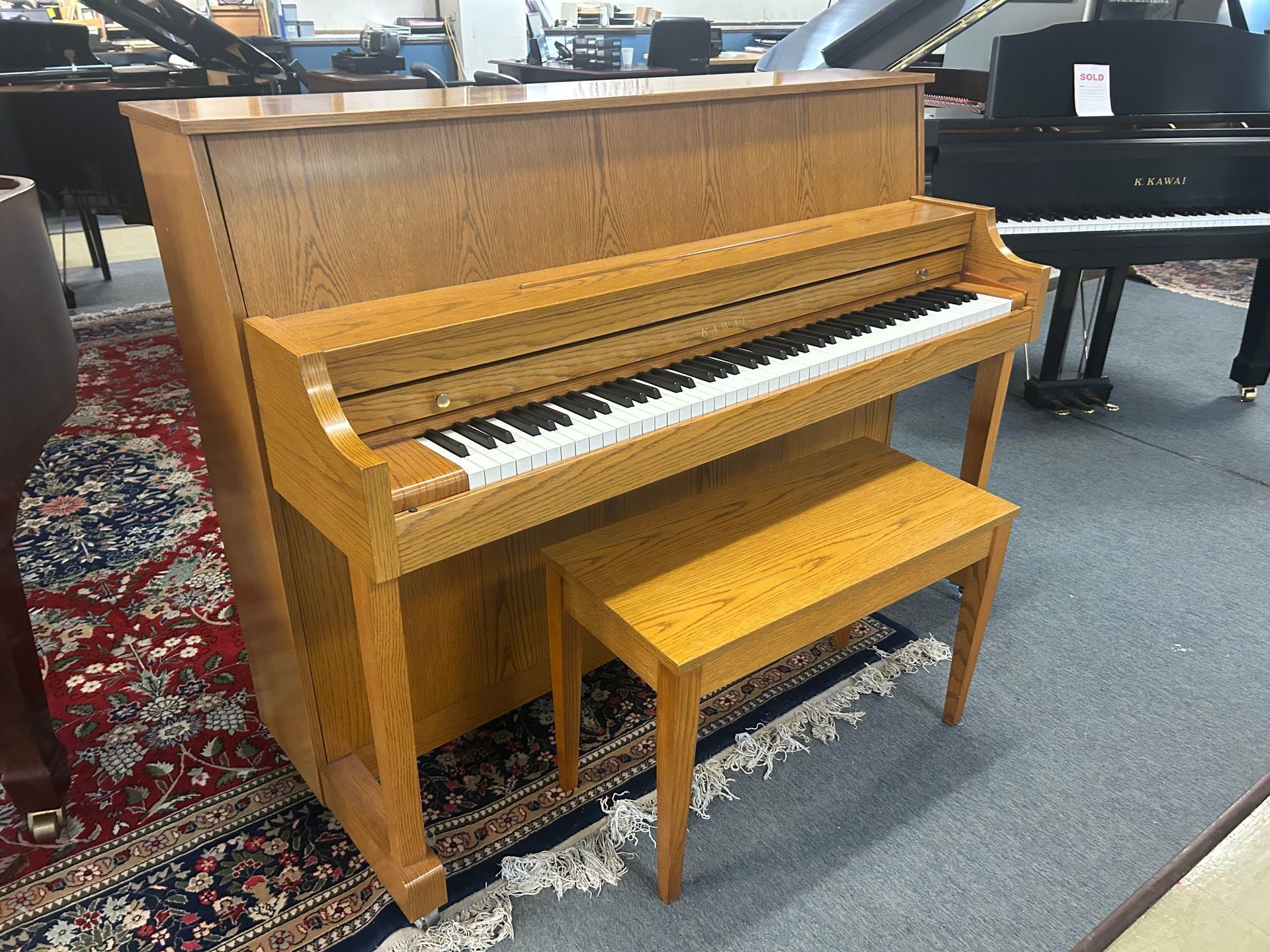 Wooden upright piano with matching bench on patterned rug.
