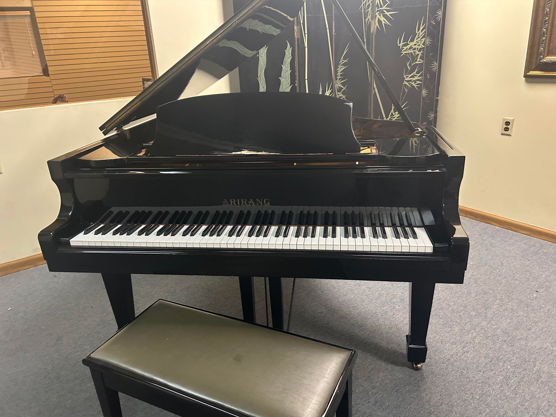 Black grand piano with bench, inside a room.