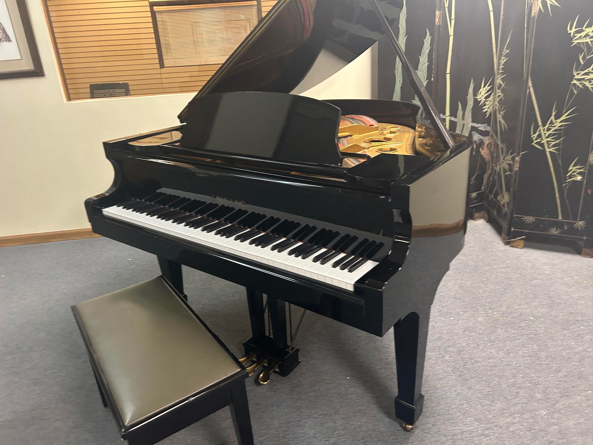 Black grand piano with a matching bench in a room with patterned wallpaper.