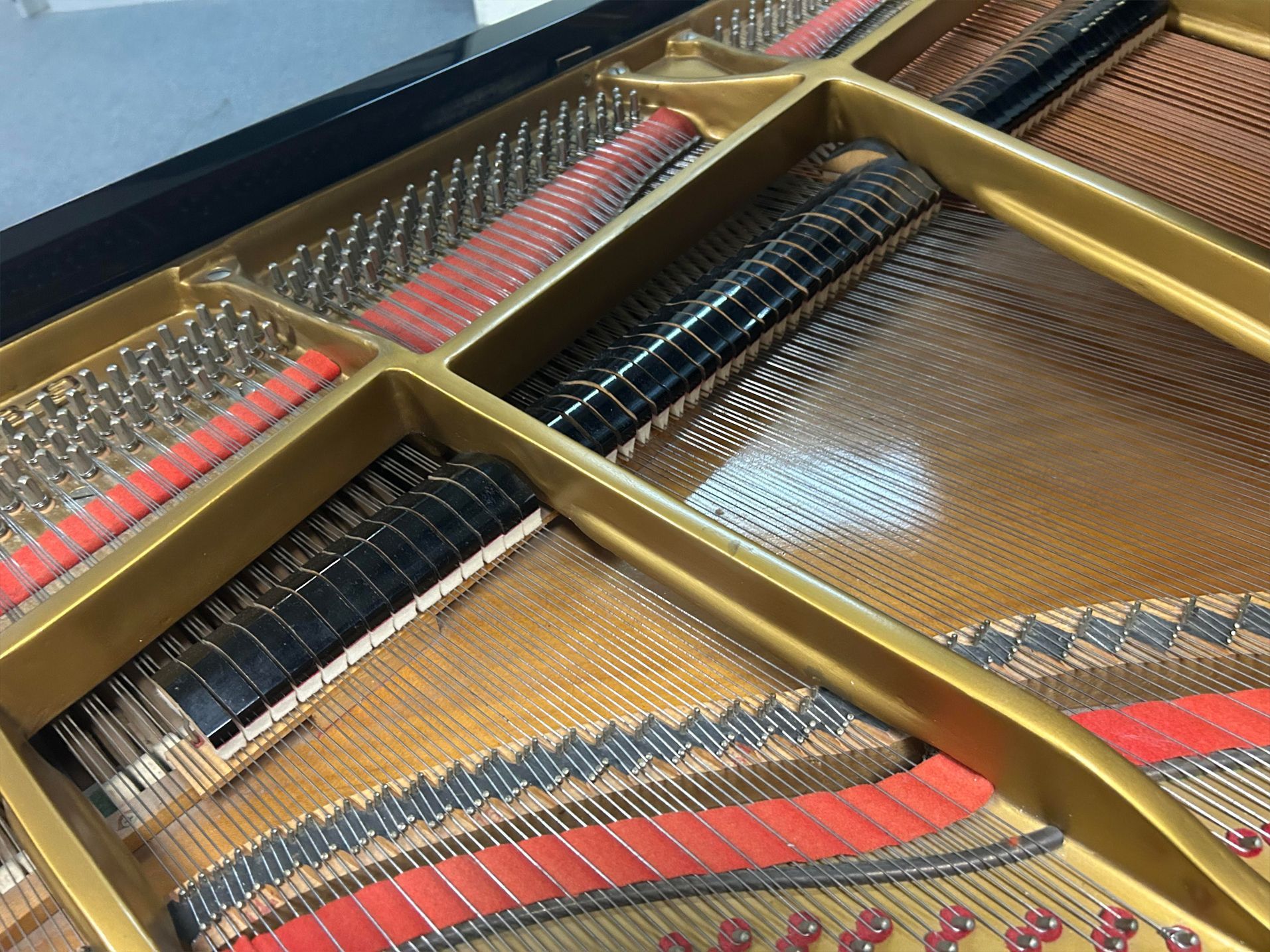 Interior view of a grand piano showing strings, soundboard, and golden structural supports.