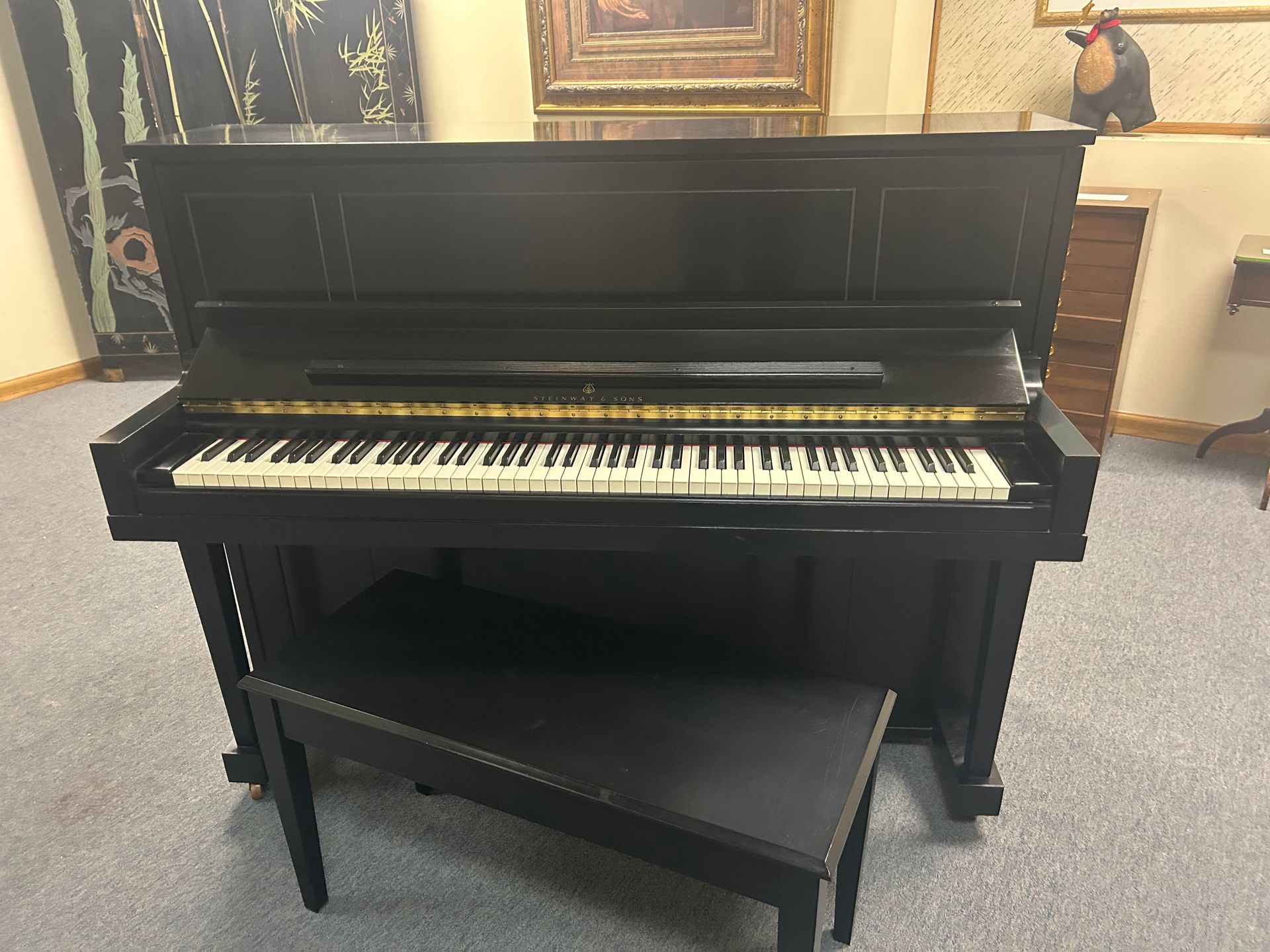 Black upright piano with bench in a room with artwork.