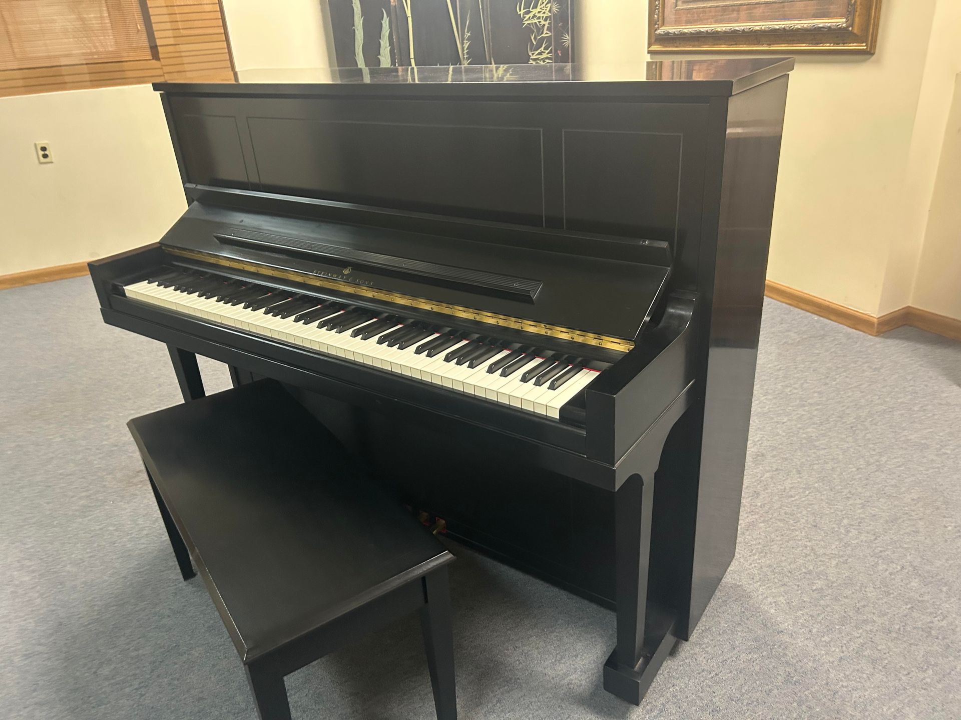 Black upright piano and matching bench in a room with light-colored walls and carpet.