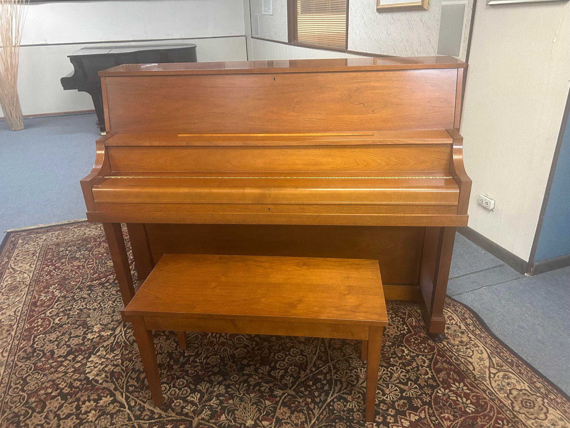A piano with a bench underneath it is sitting on a rug in a room.
