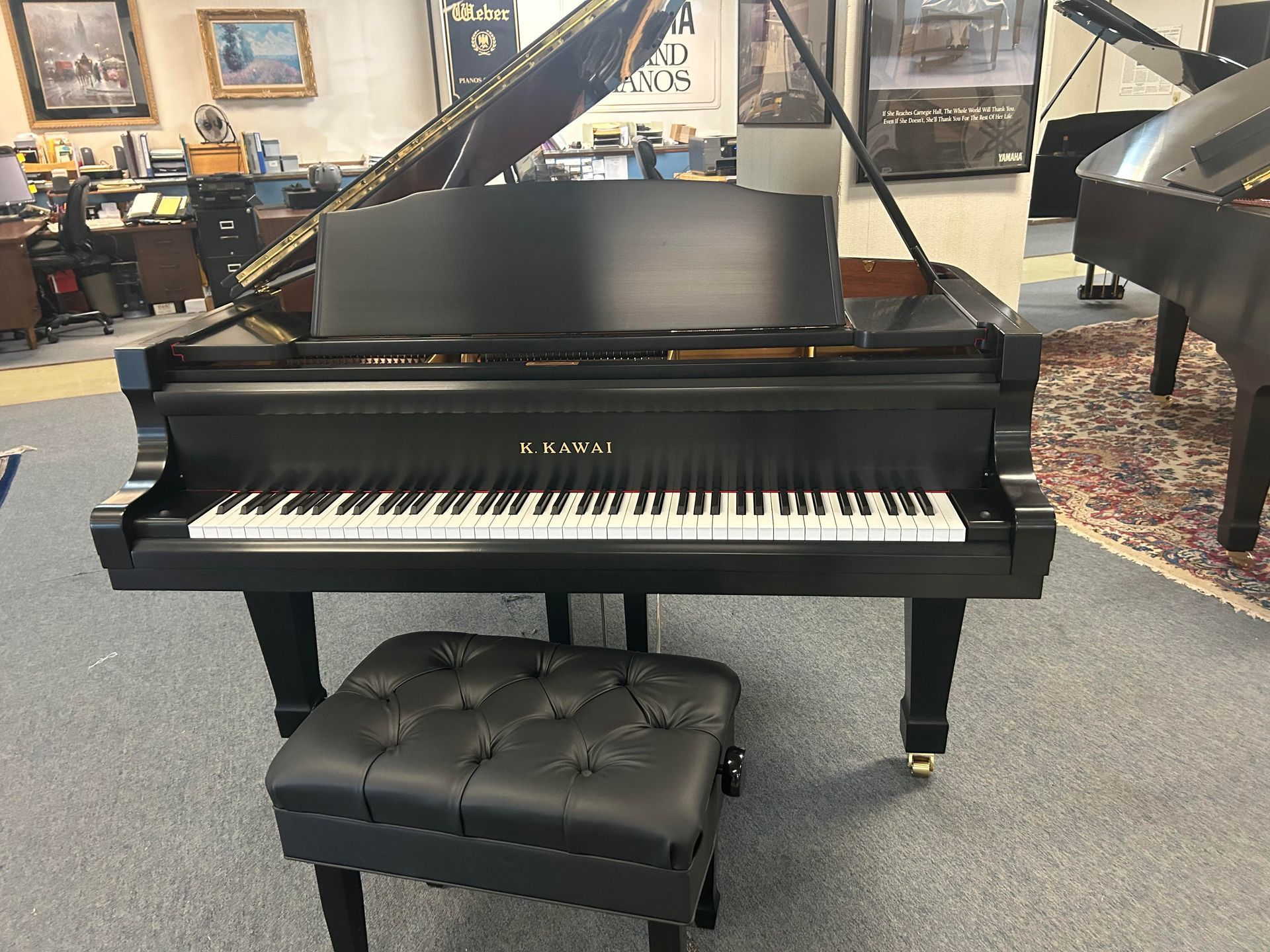 Black grand piano with a black leather bench in a room.
