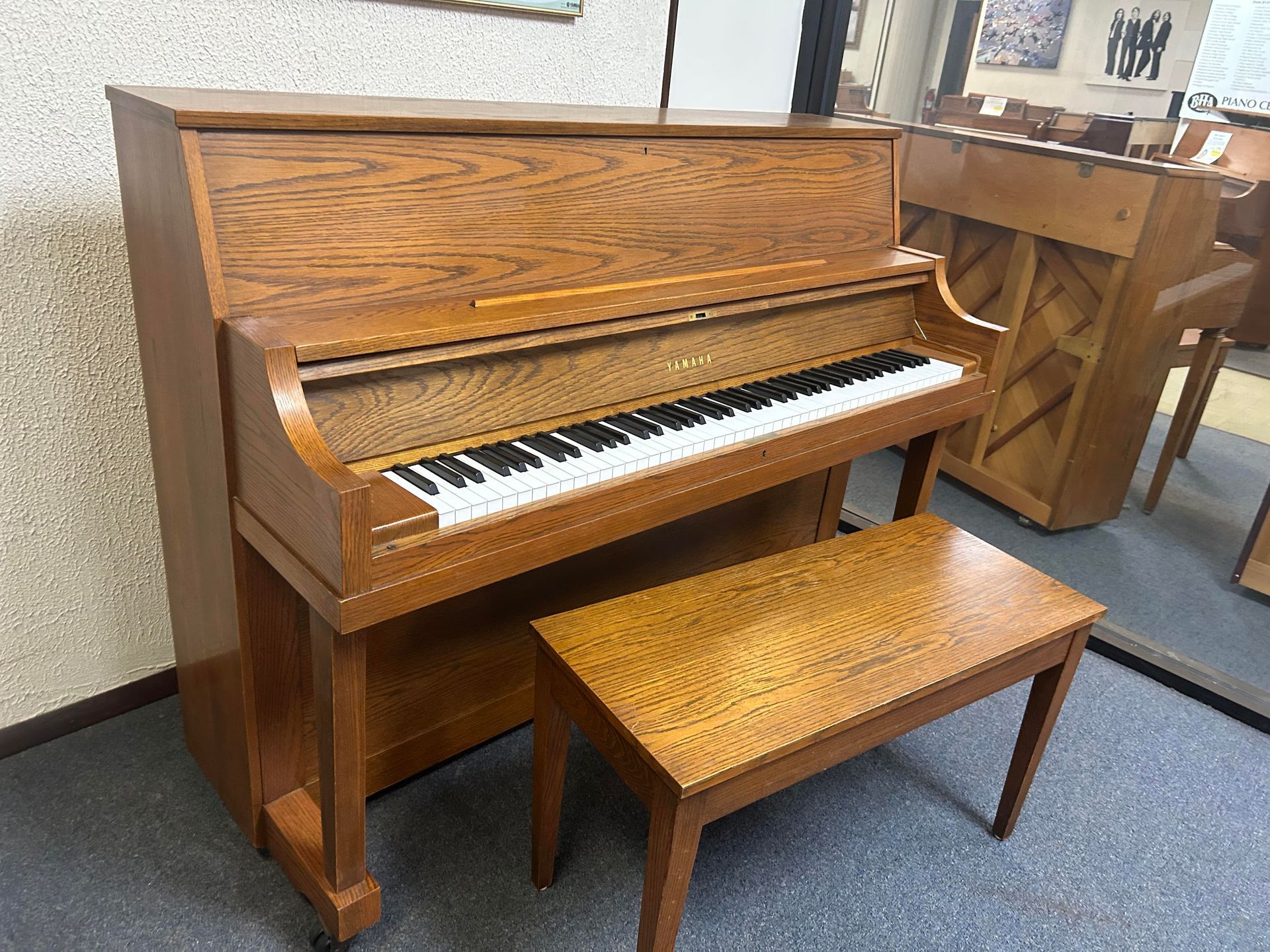 Upright wooden piano with bench in a room; warm wood tones.