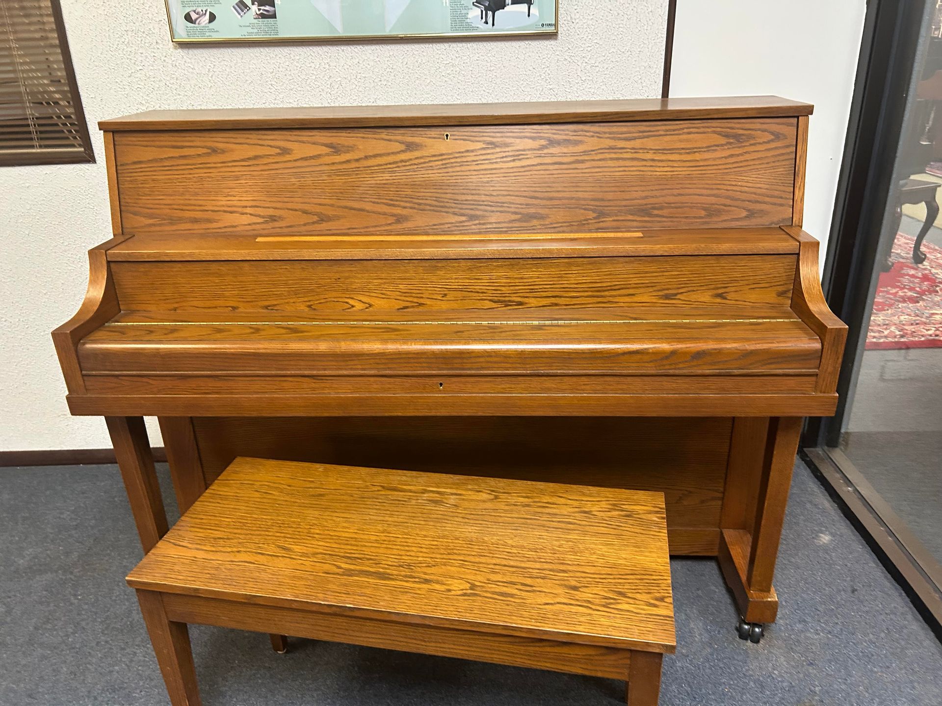 Wooden upright piano with matching bench, set in a room.
