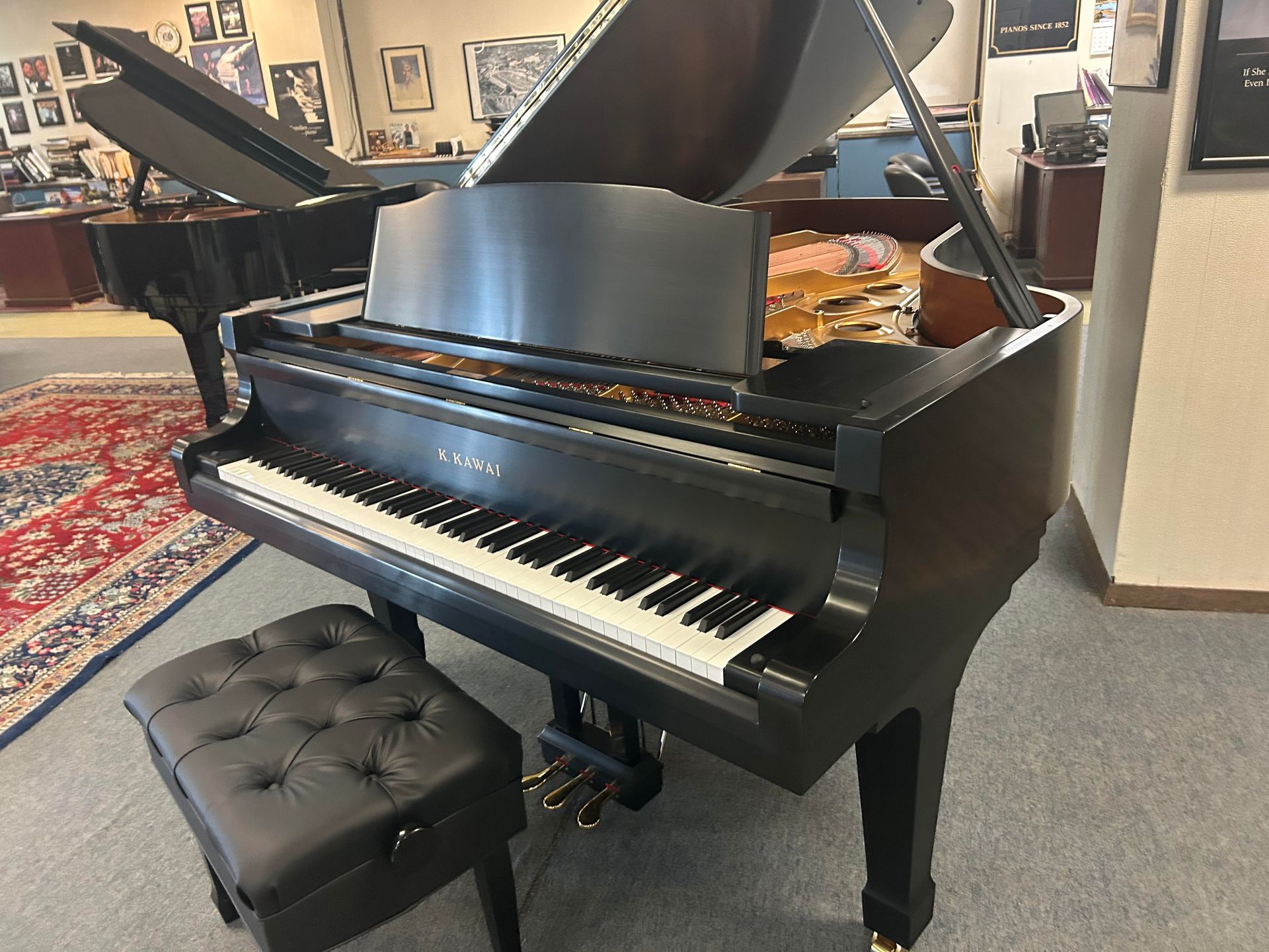 Black grand piano with a black leather bench in a showroom.