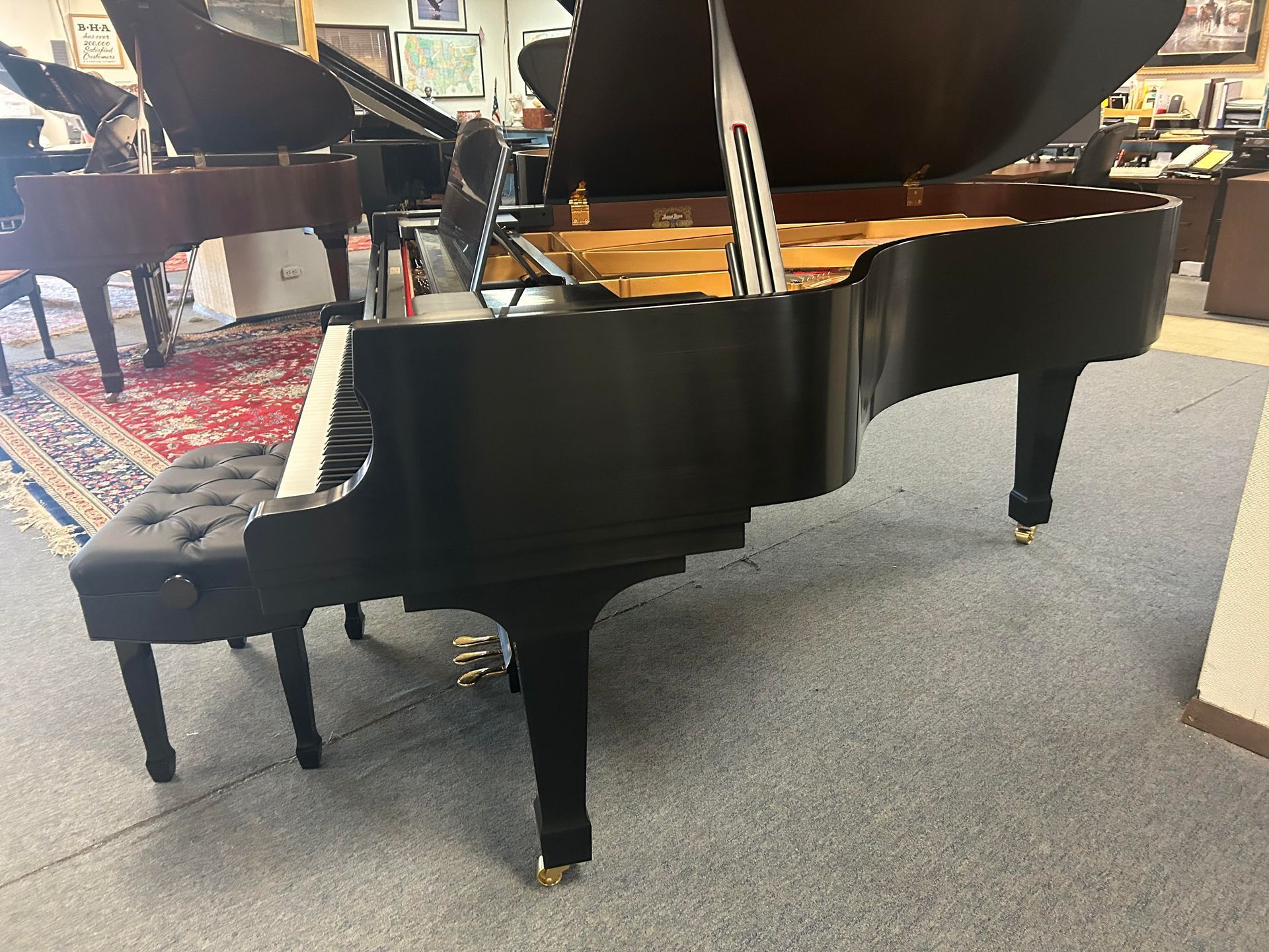 Black grand piano in a showroom with a black bench.