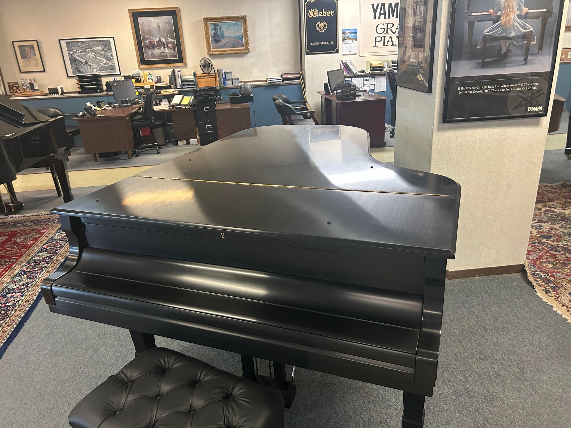 Black grand piano with a black cushioned stool in a showroom.