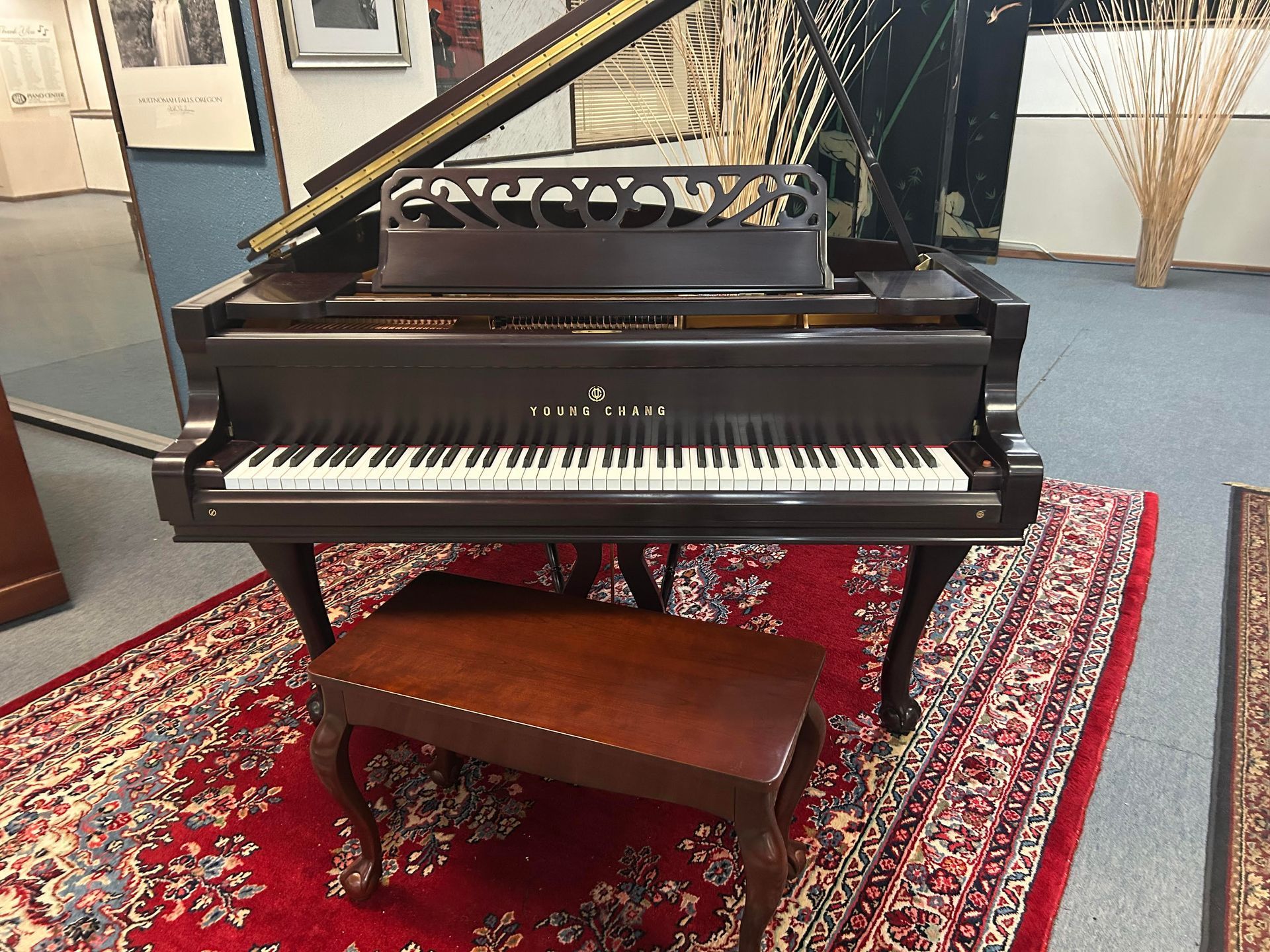 A piano is sitting on a rug next to a bench.