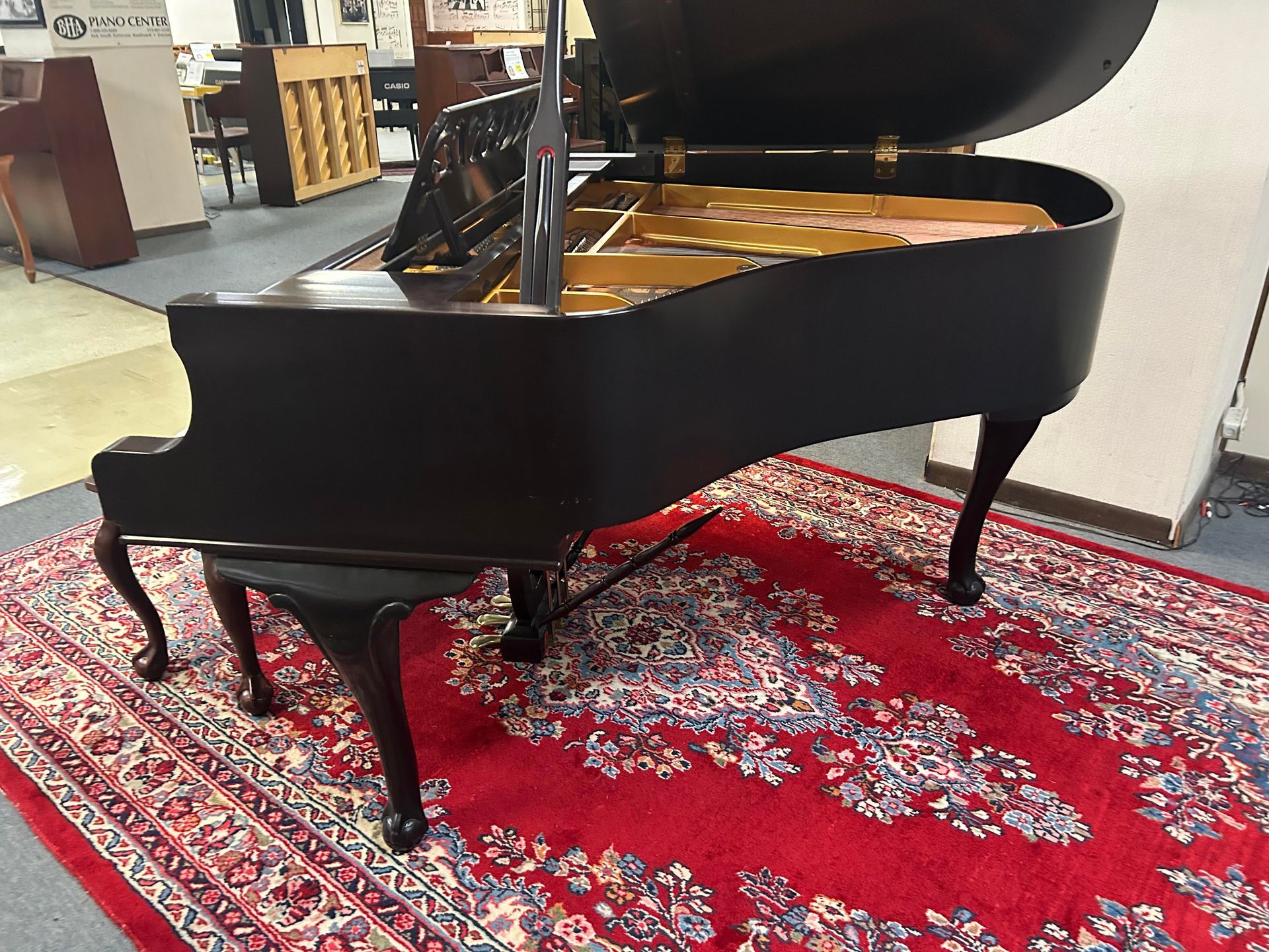 A black grand piano is sitting on a red rug.