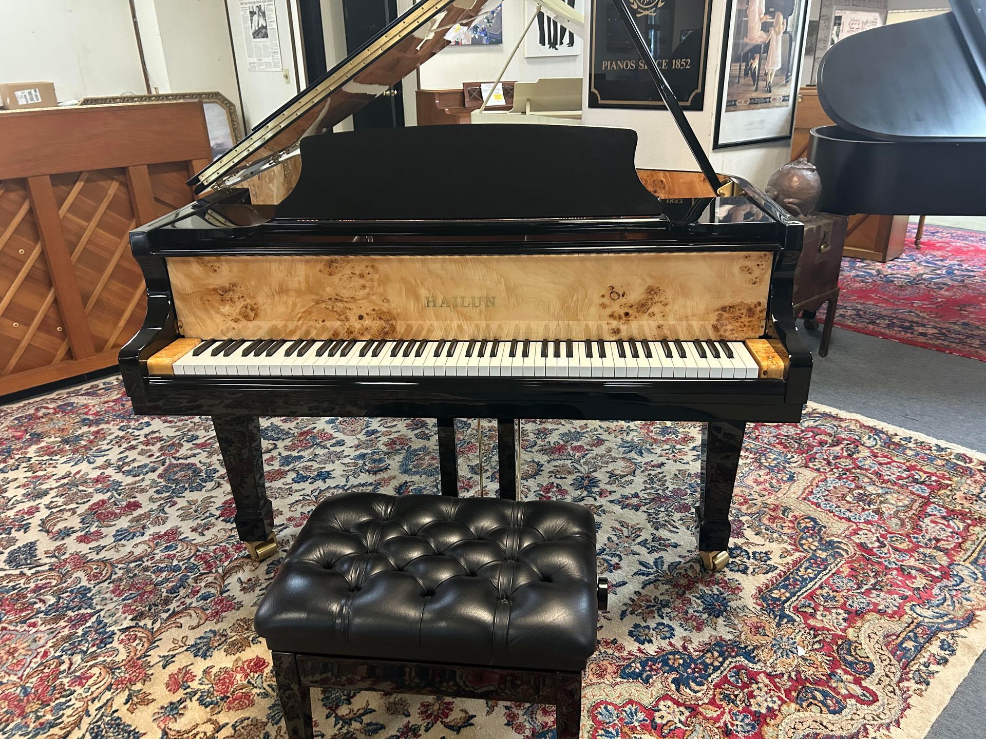 Grand piano with a black frame and a natural wood grain front, on a patterned rug, with a matching leather bench.