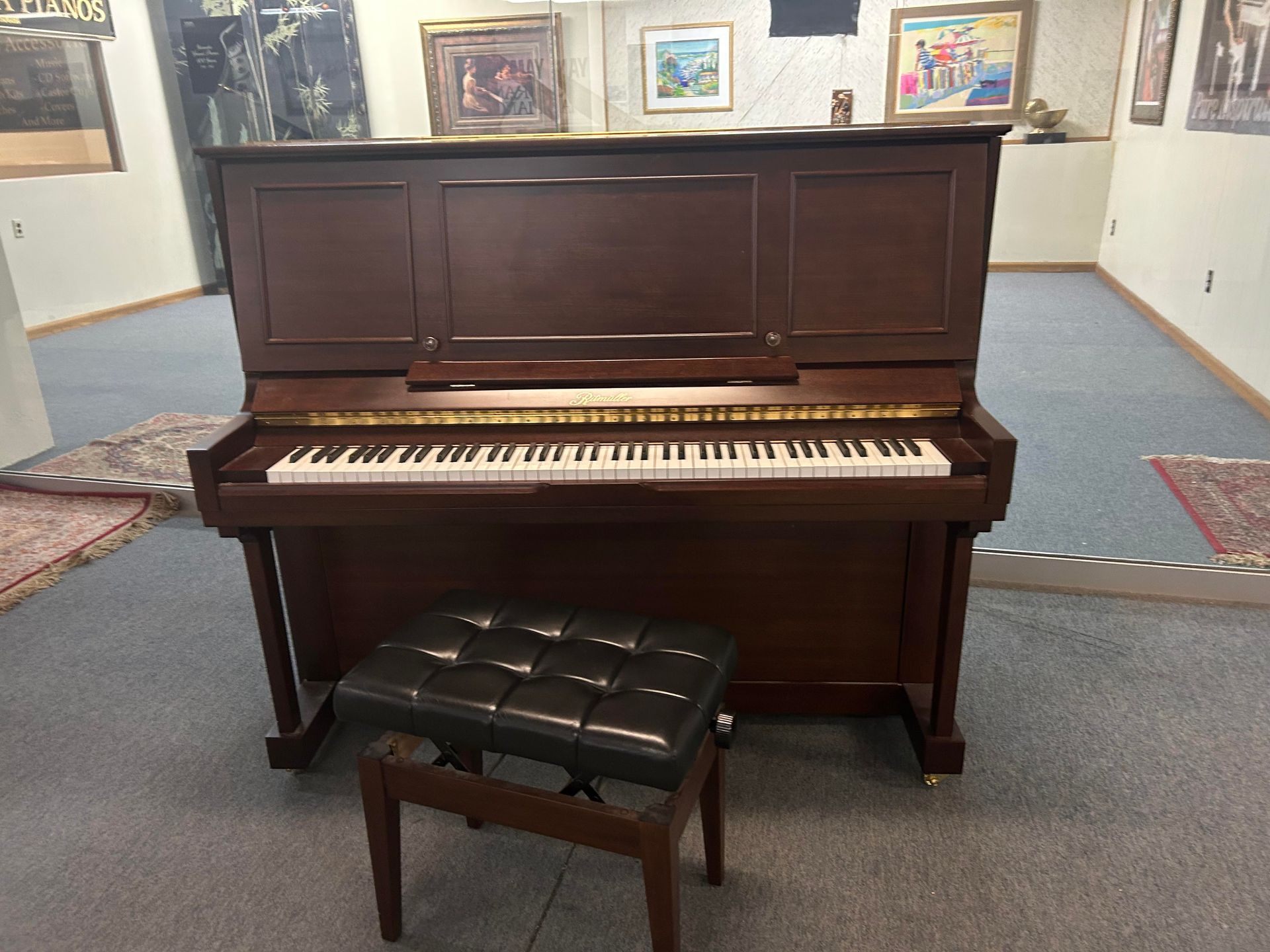 Upright brown piano with a black bench in a room with artwork on the walls.