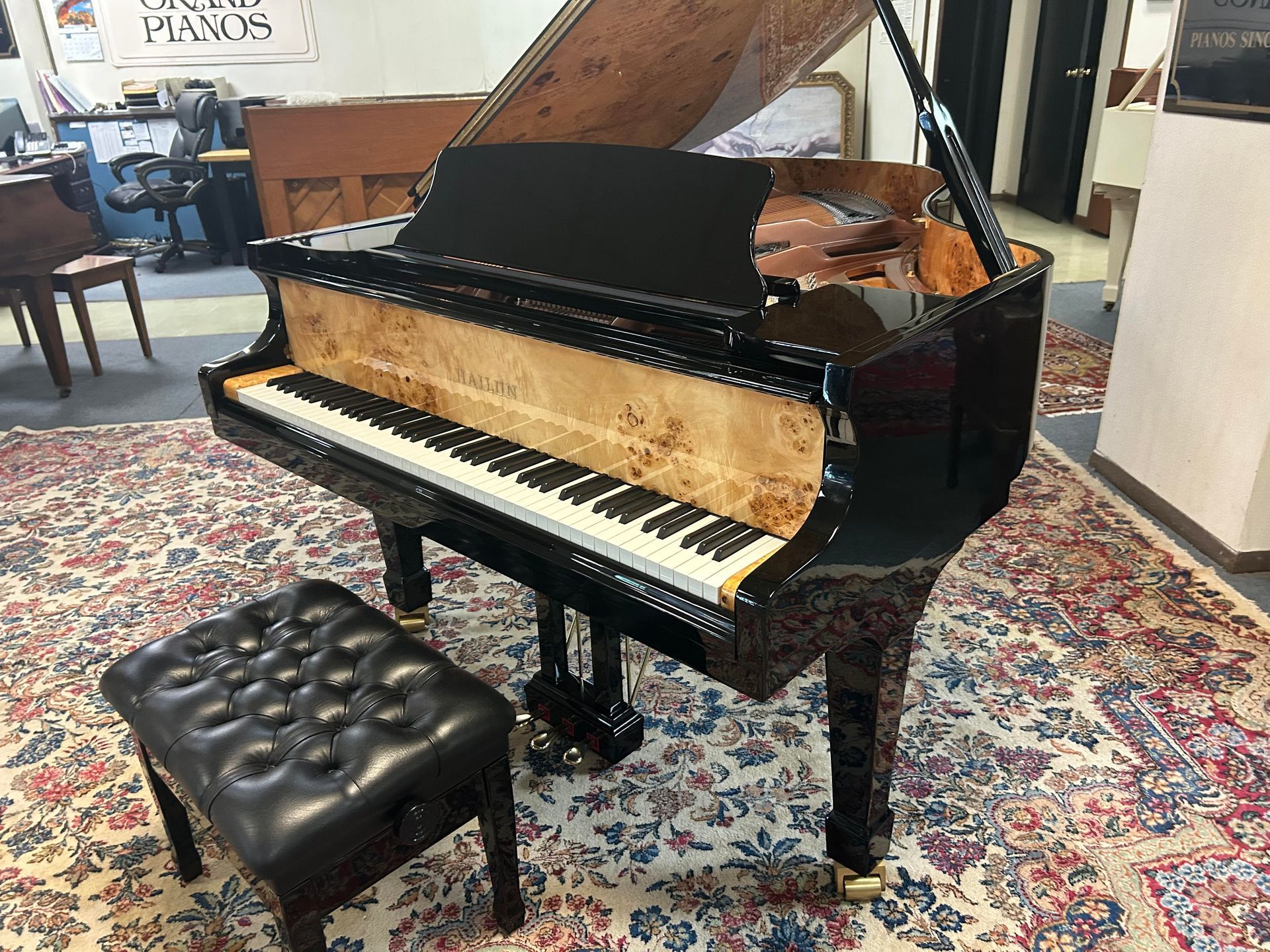 Black grand piano with burl wood accents on a patterned rug, near a black leather piano bench.