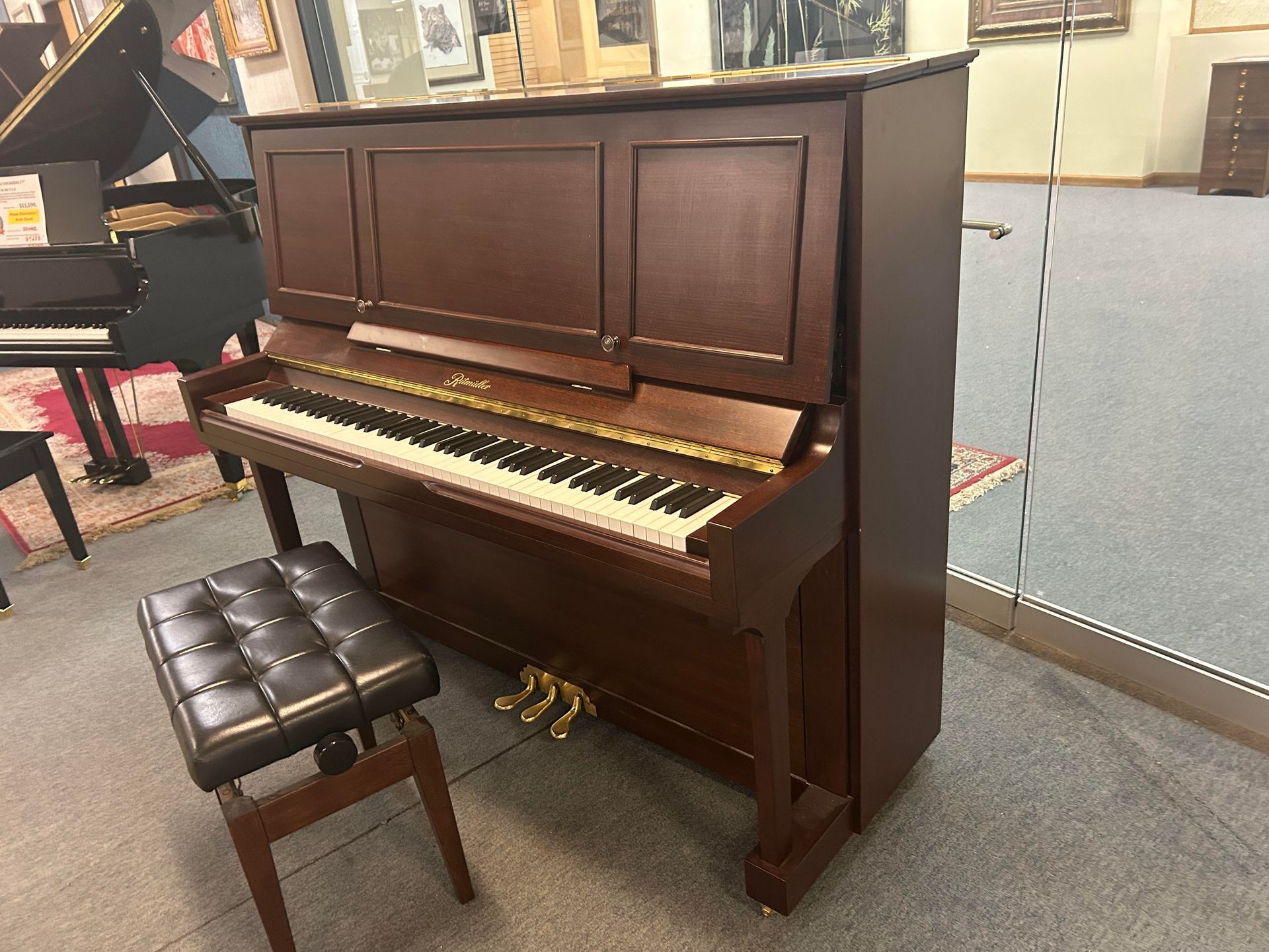 Upright brown piano with a black seat in a showroom.