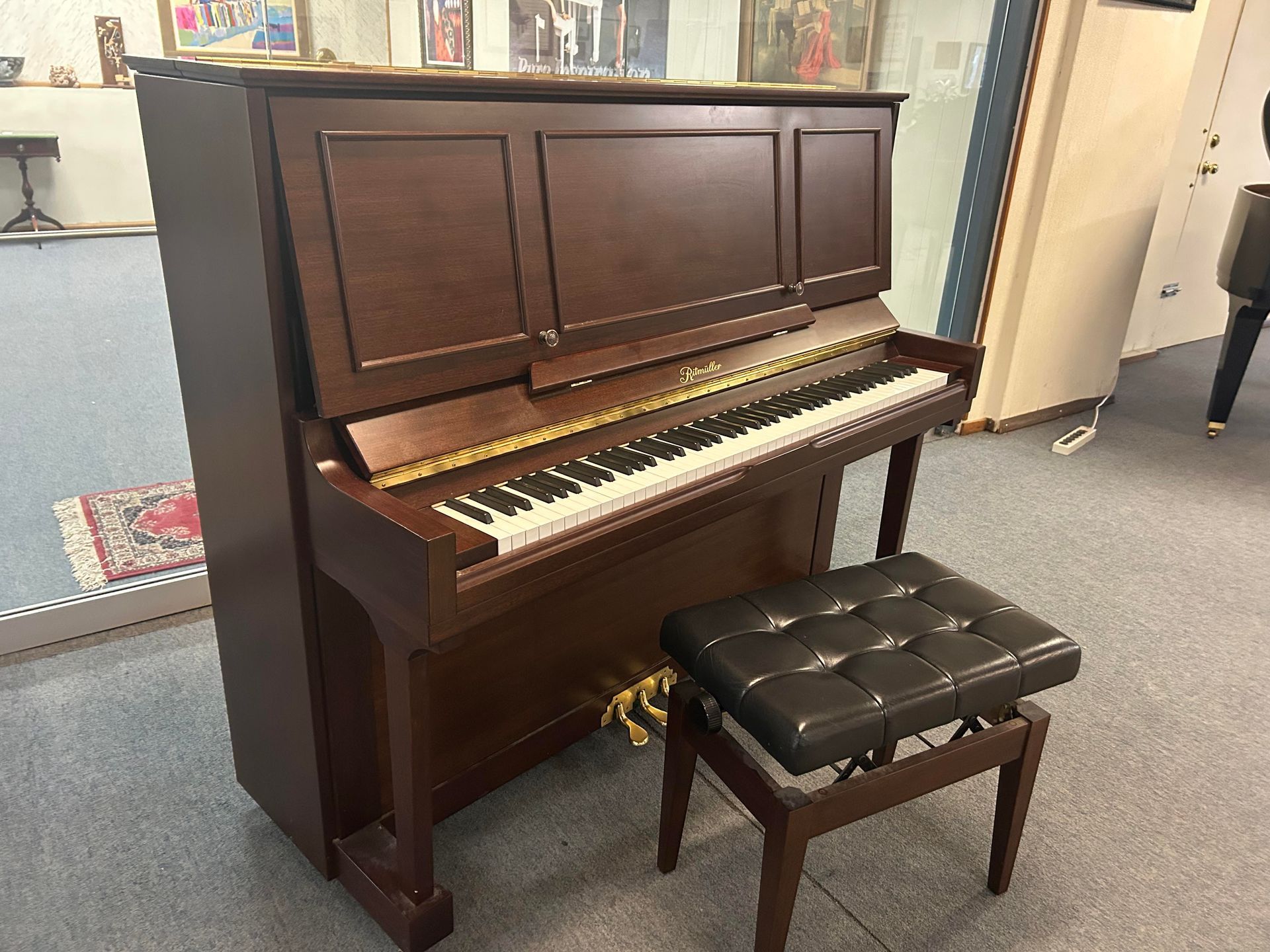 Upright brown piano with a black padded bench in a room with a rug.