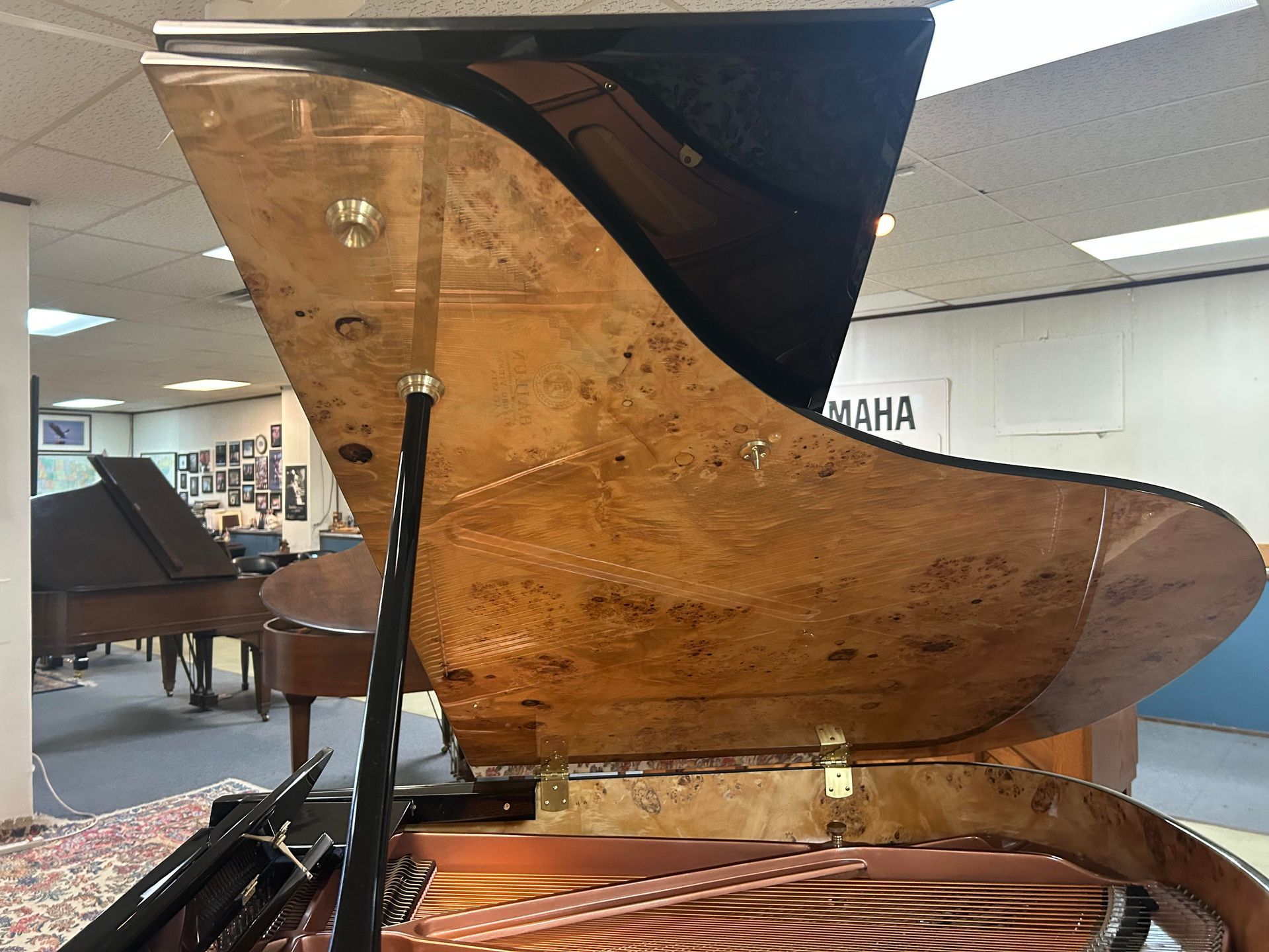 A grand piano with its top open, showcasing the interior wood grain. Another piano and a