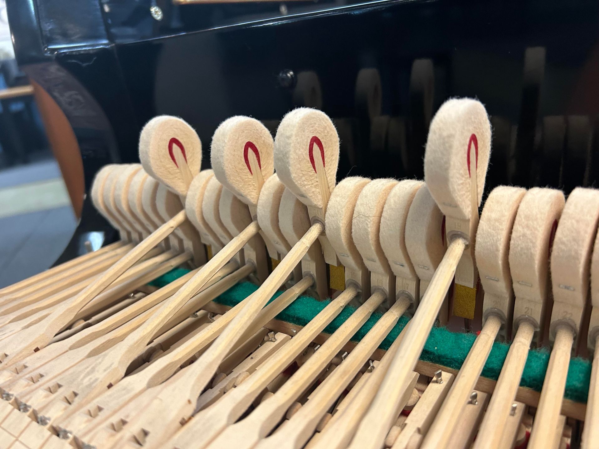 Close-up of piano hammers, with felt striking surfaces, resting on wooden shanks. The interior mechanism is visible.