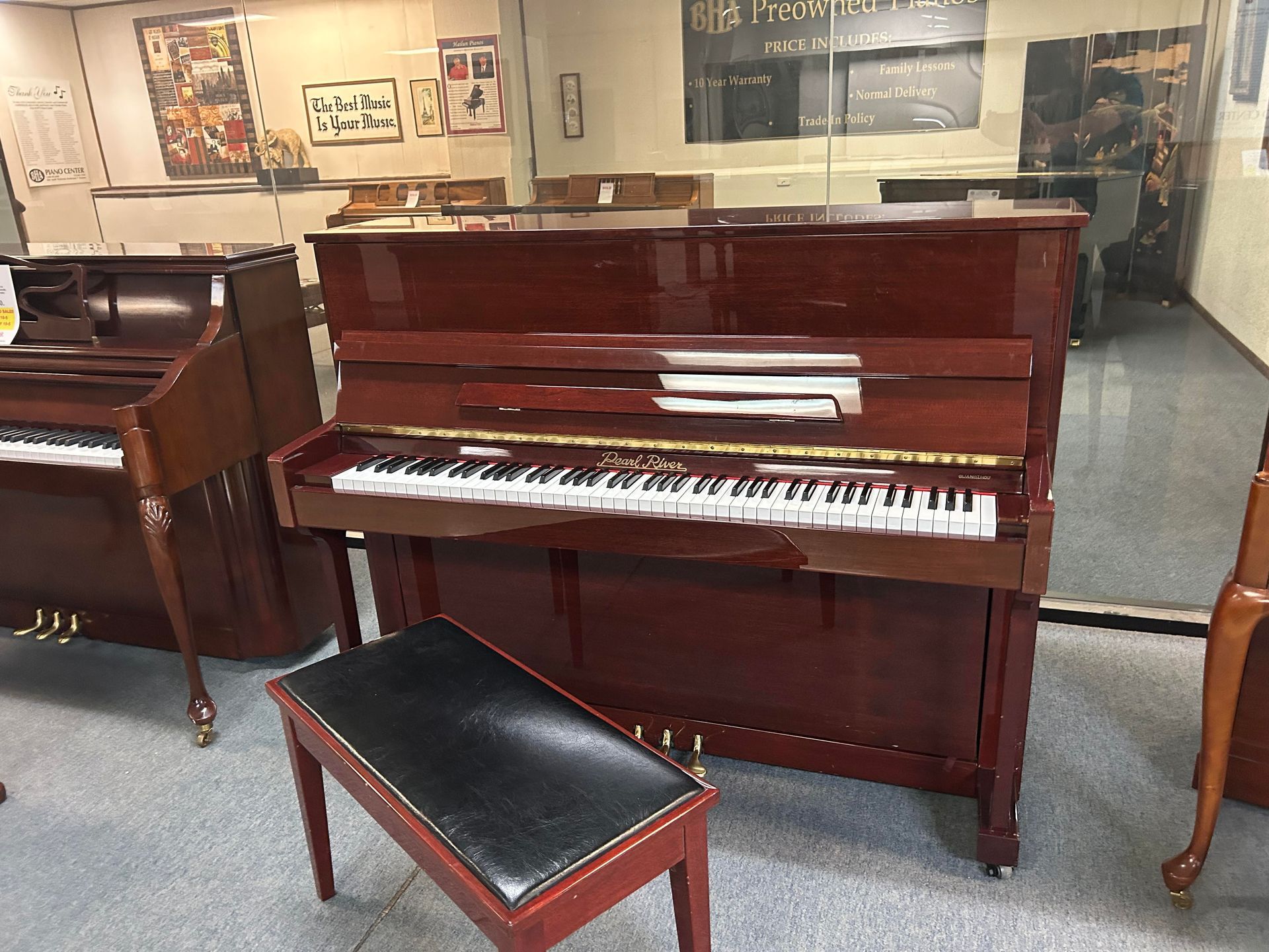 A damaged red upright piano with a matching bench in a room with other pianos.