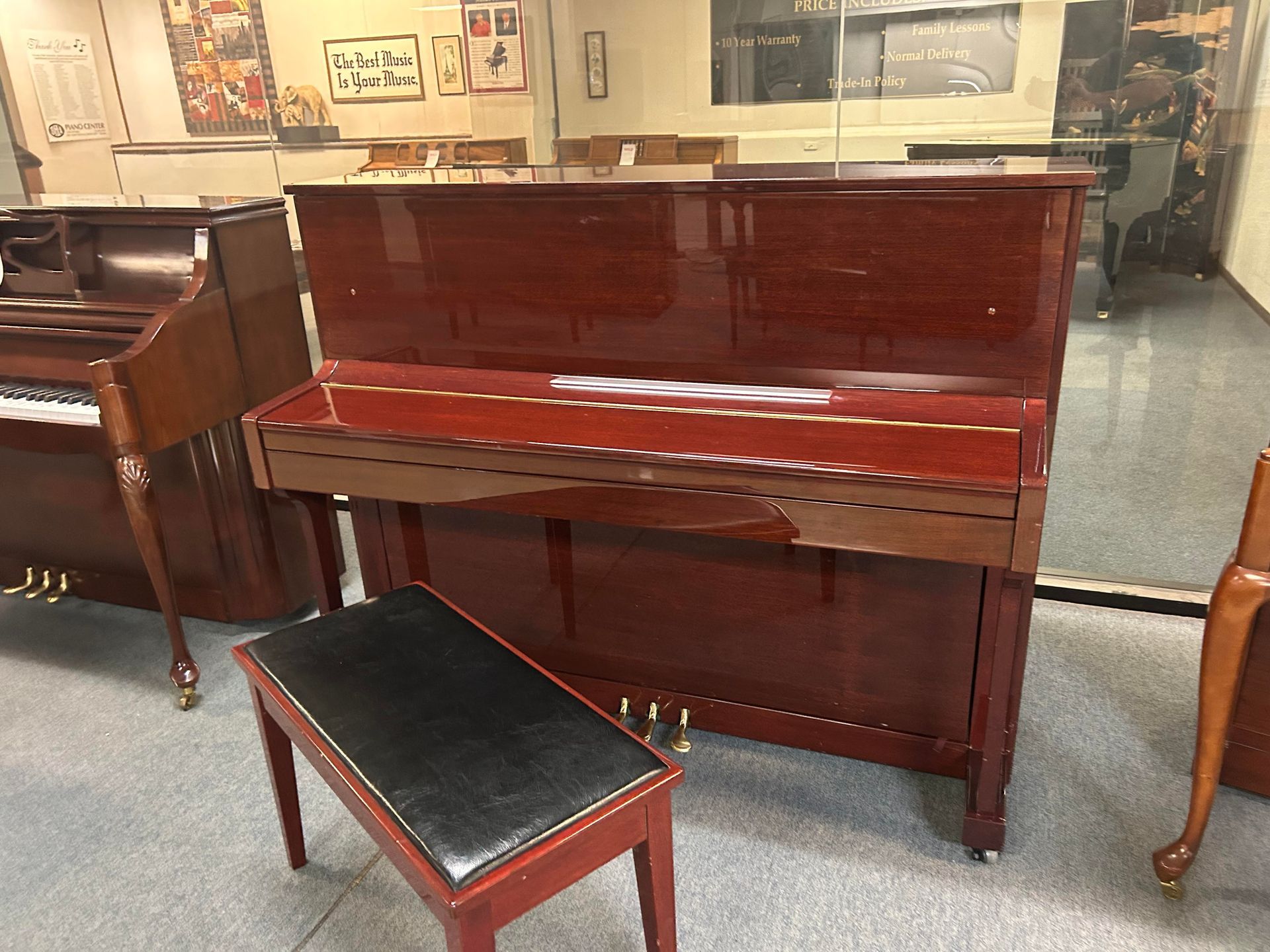 A mahogany upright piano with a black bench in a showroom. The piano has a glossy finish and the bench is in front.