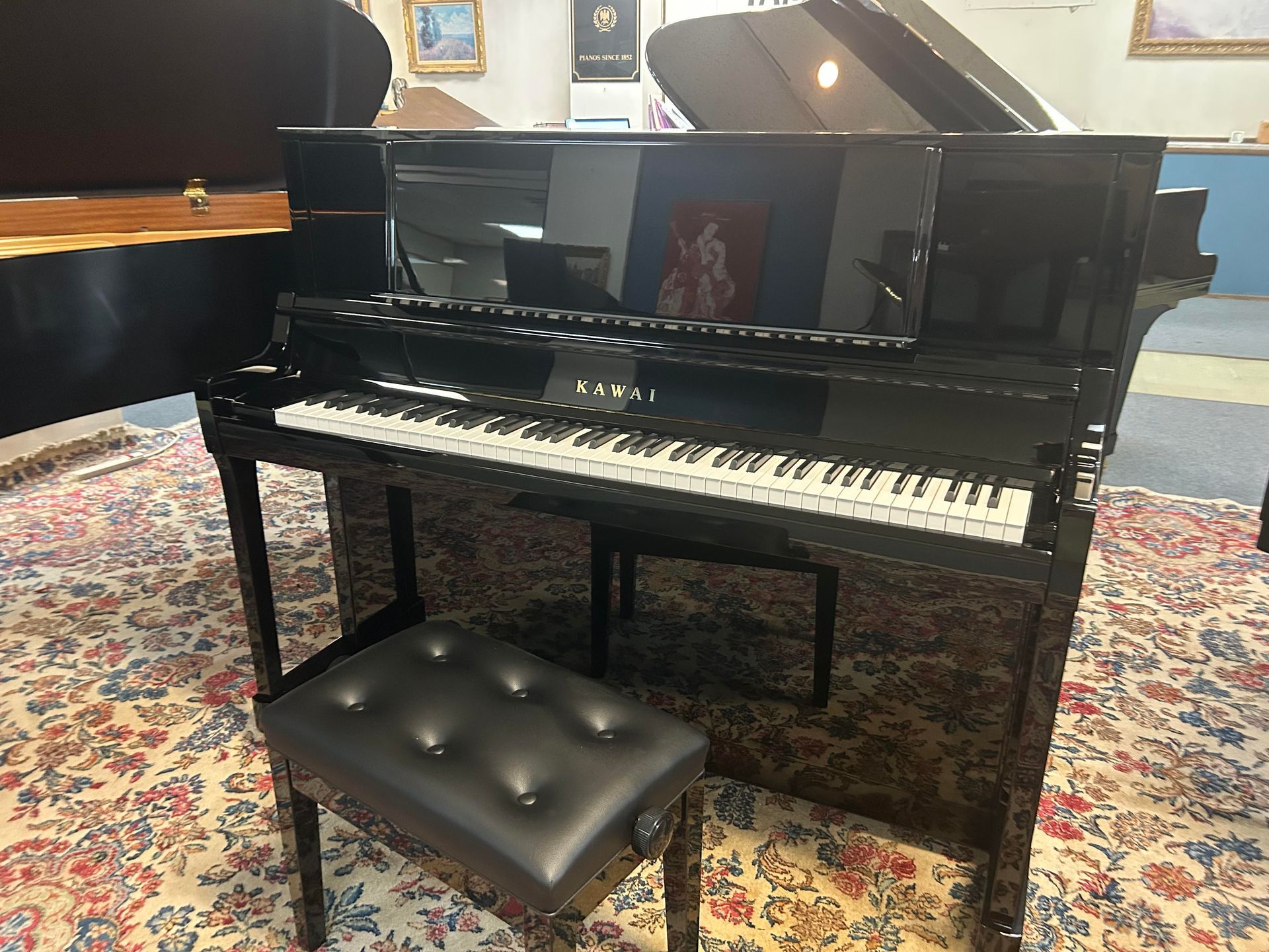 Black upright piano with matching bench in a showroom setting.