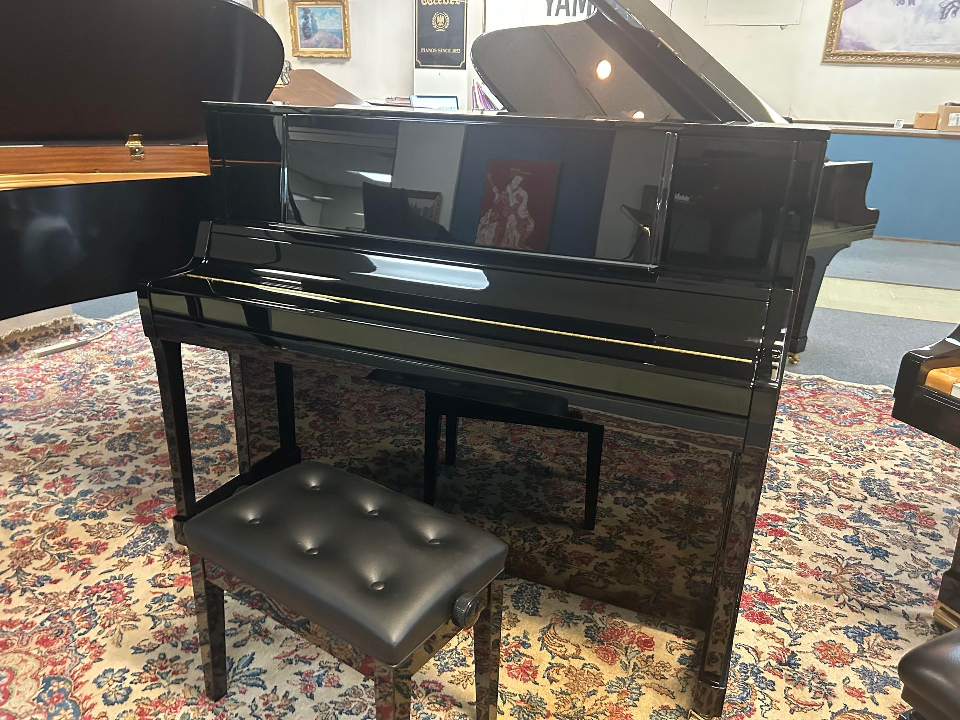 Black upright piano with matching stool on a patterned rug.