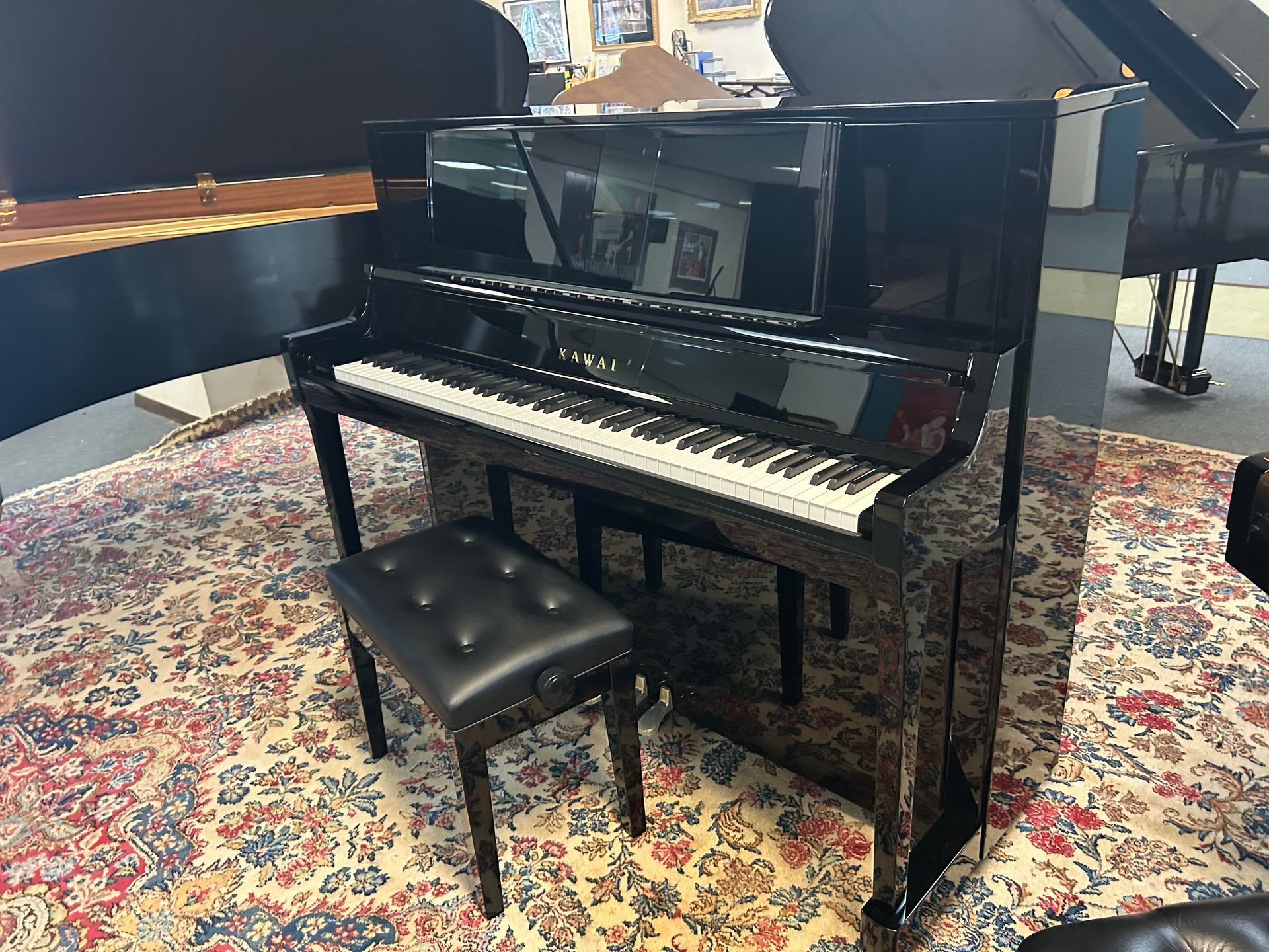 Black upright piano with matching bench on a patterned rug in a showroom.