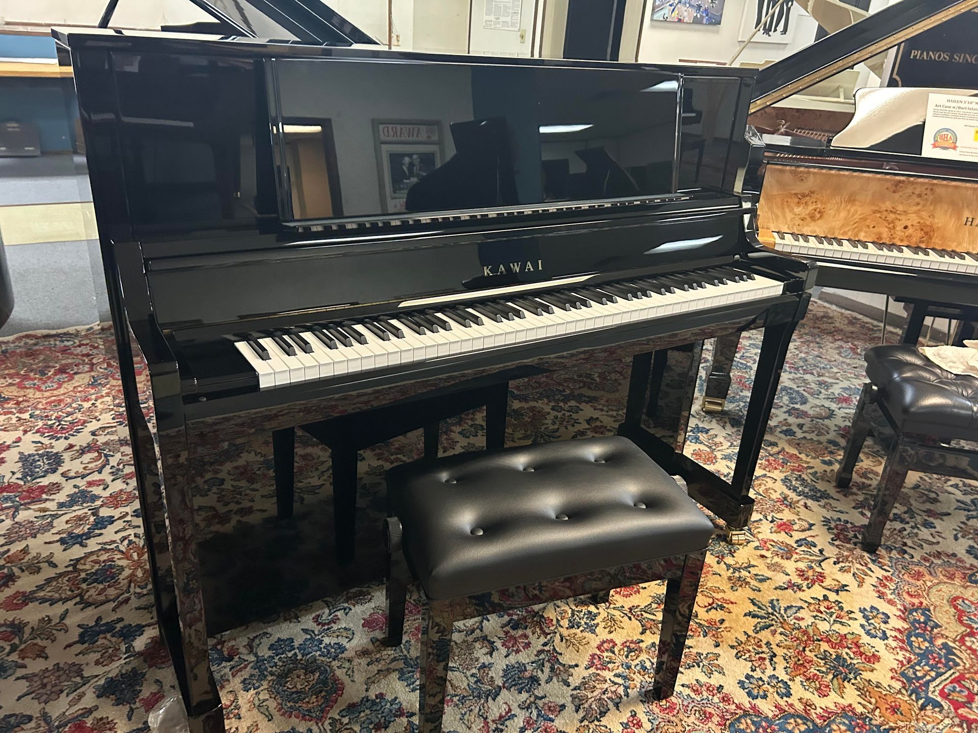 Black Kawai upright piano with bench on patterned rug.