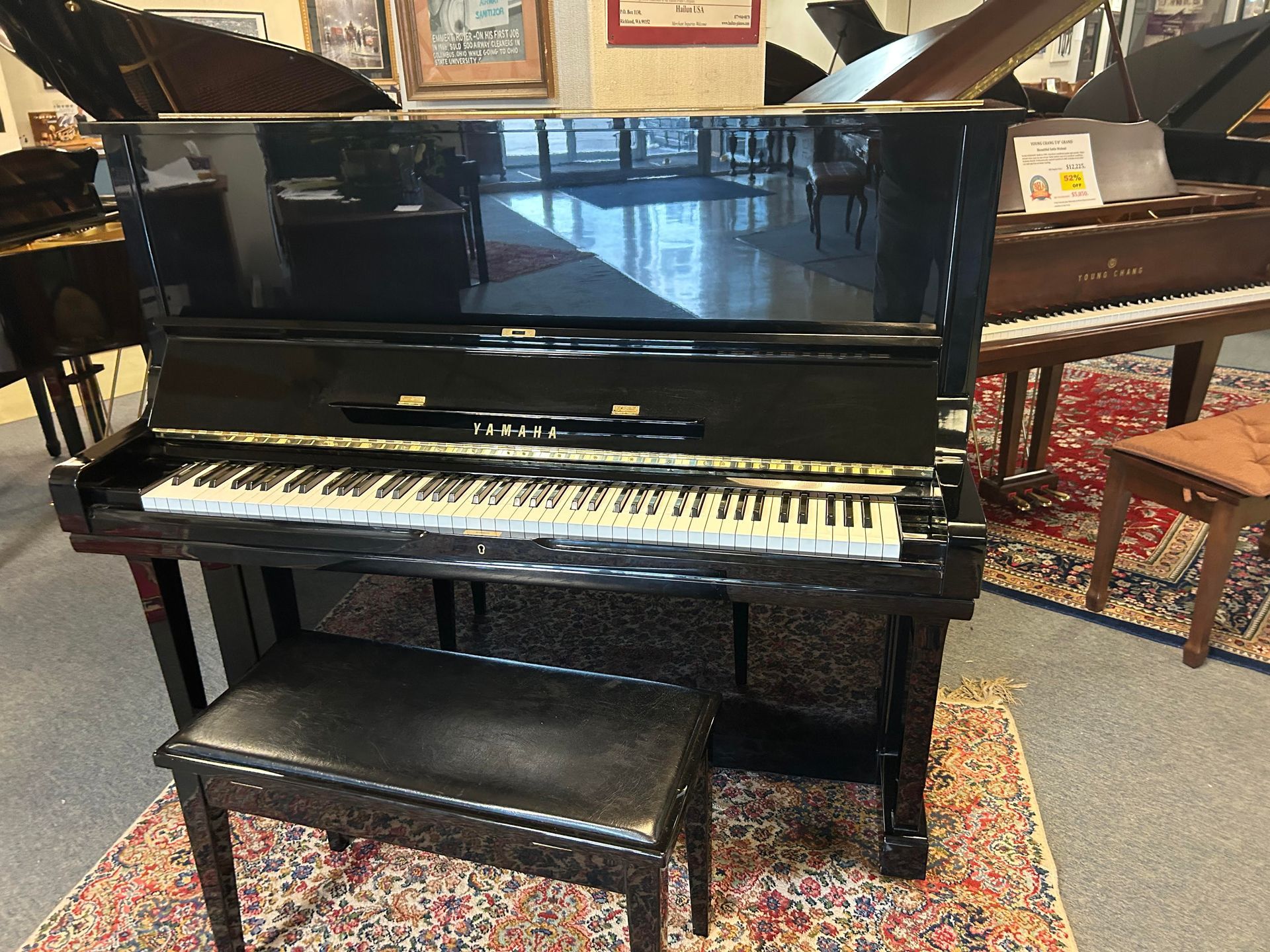 A black piano is sitting on a rug in a room with other pianos.