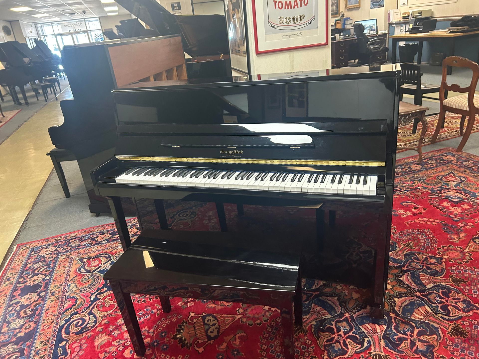A black upright piano with a matching bench sitting on a patterned red rug in a showroom.