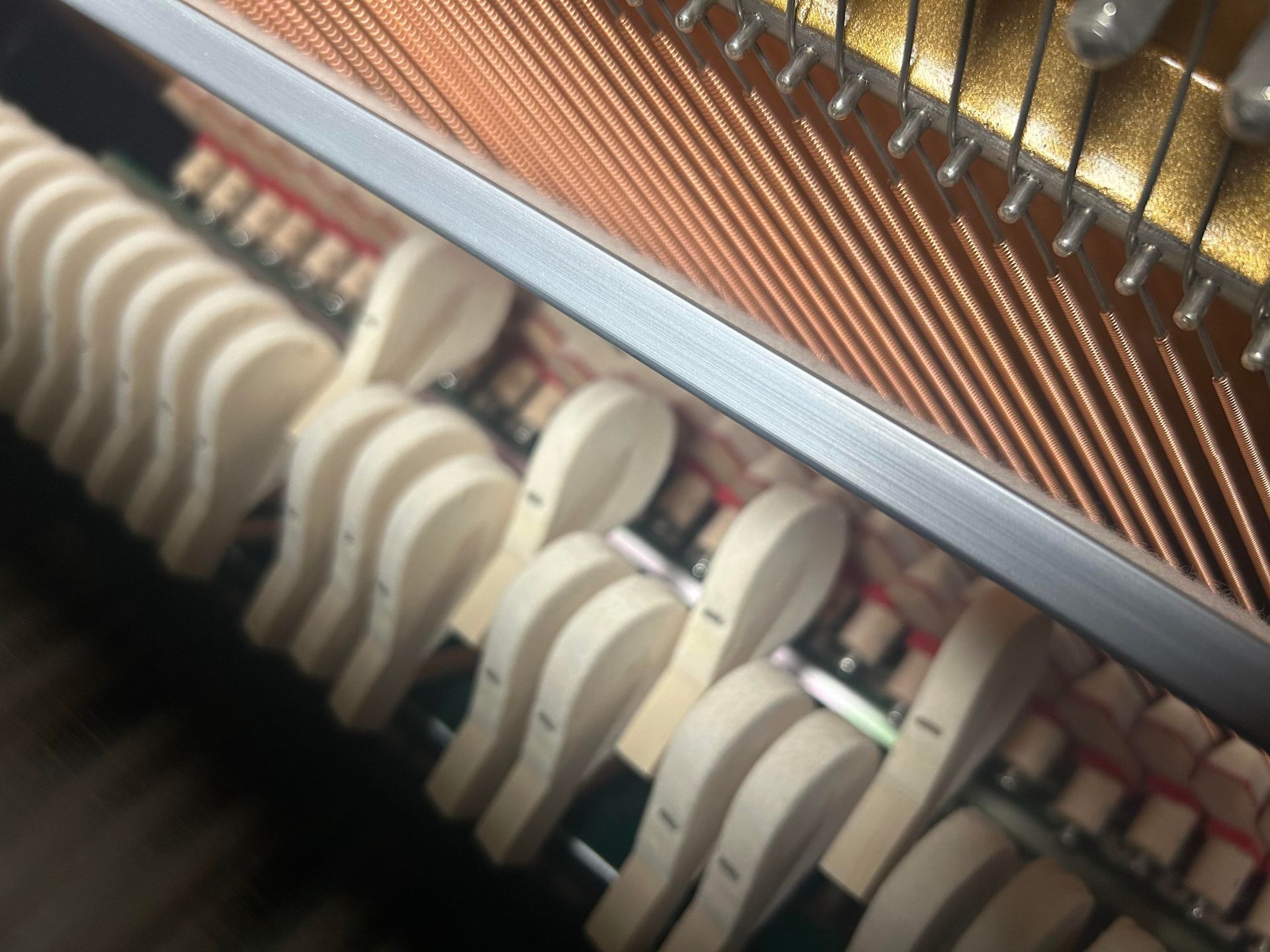 A close-up view of a piano's internal hammer mechanism with felt-covered hammers positioned beneath metal strings.
