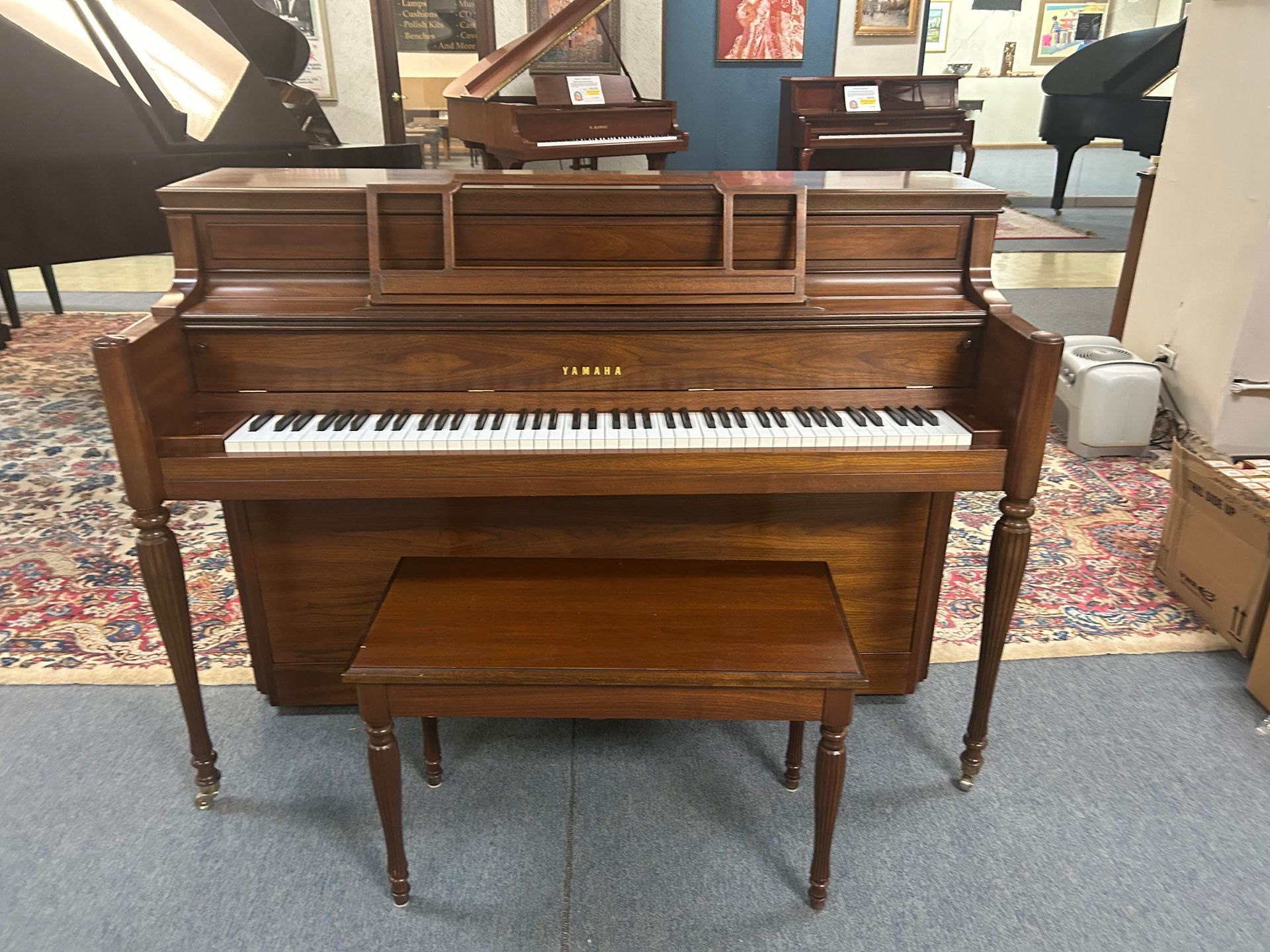 Wooden Yamaha upright piano with bench in a showroom.