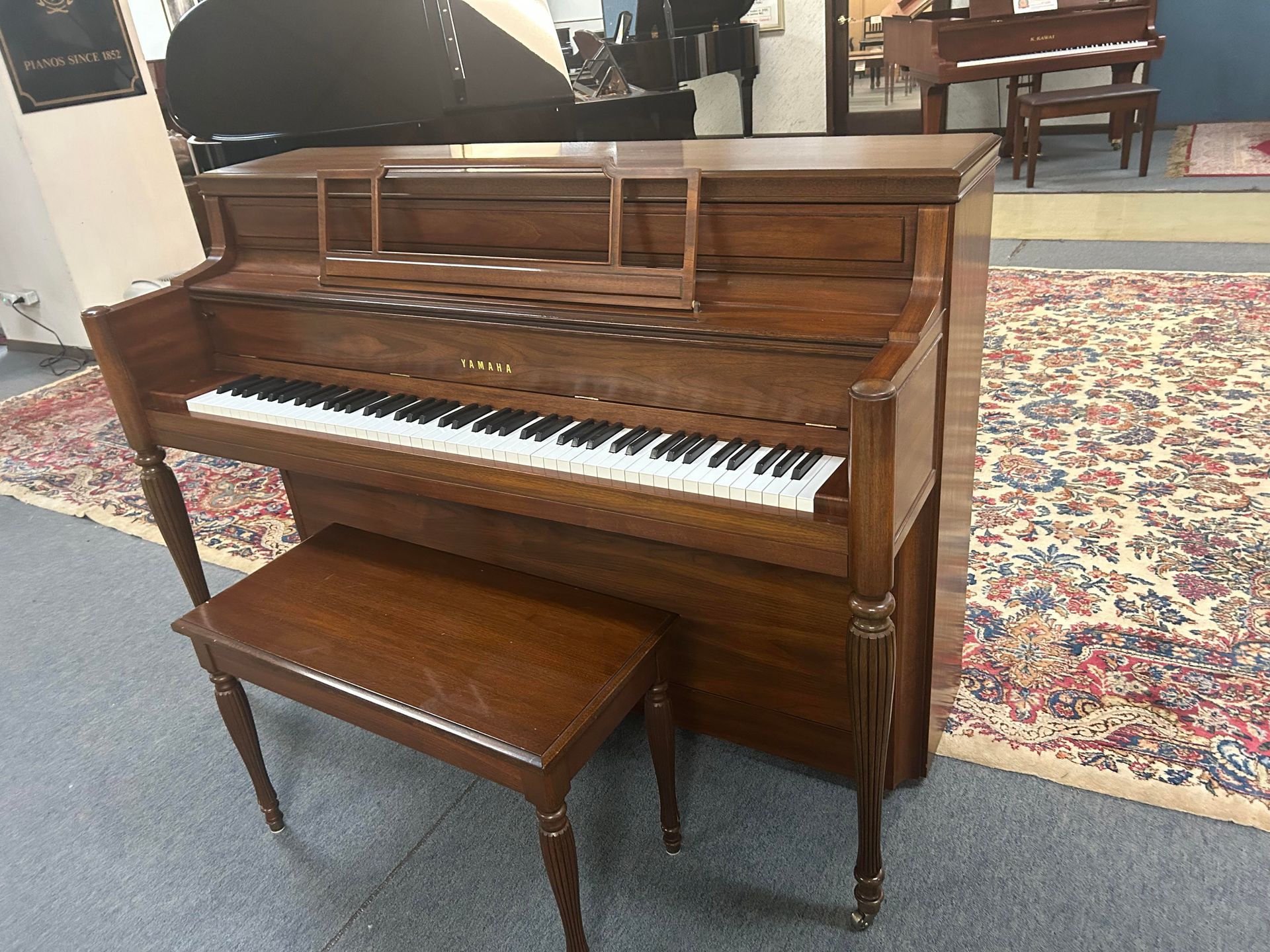 Upright brown piano with bench in a room with a patterned rug.