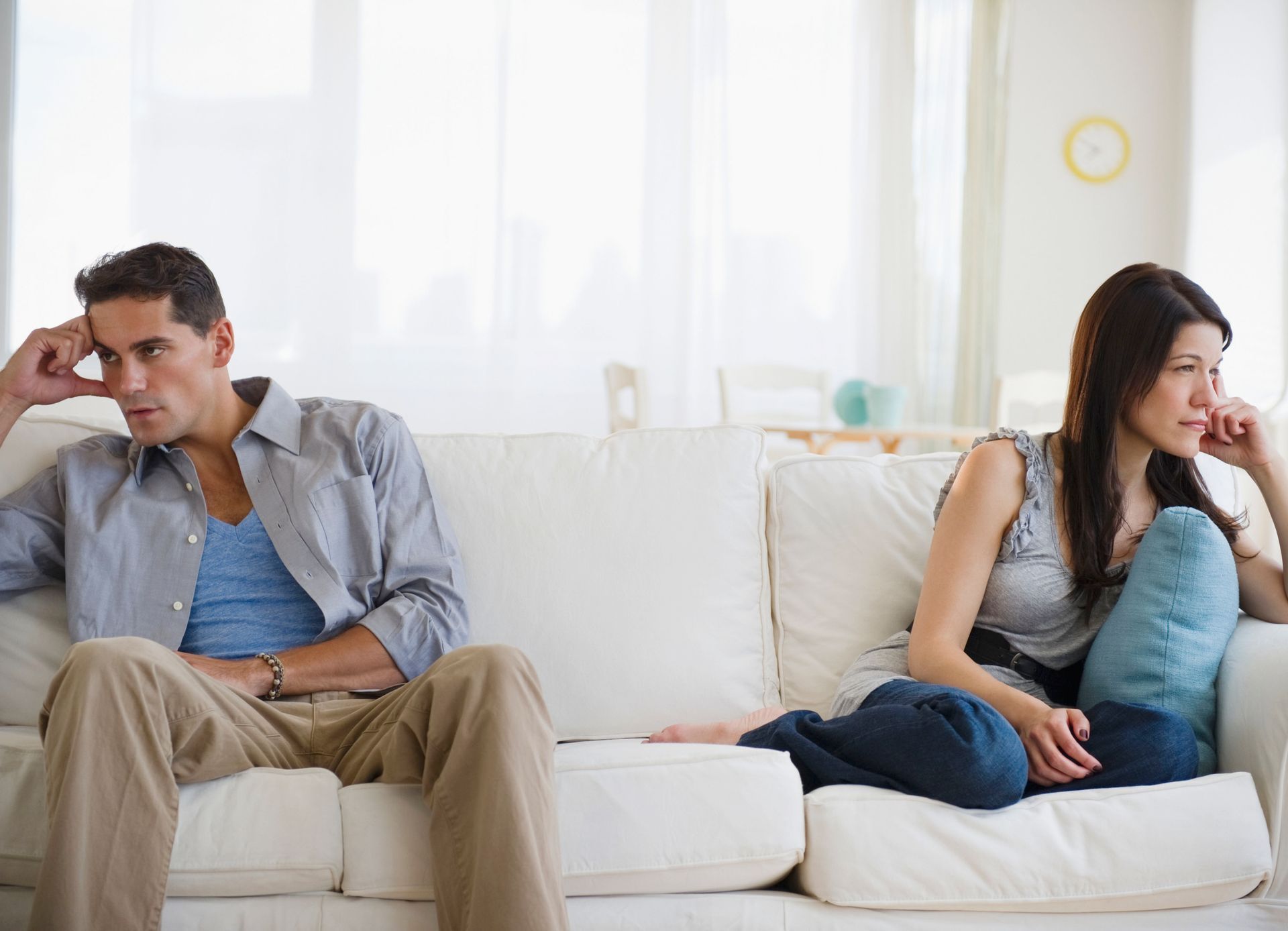 Couple sitting apart on a couch, looking away with somber expressions.