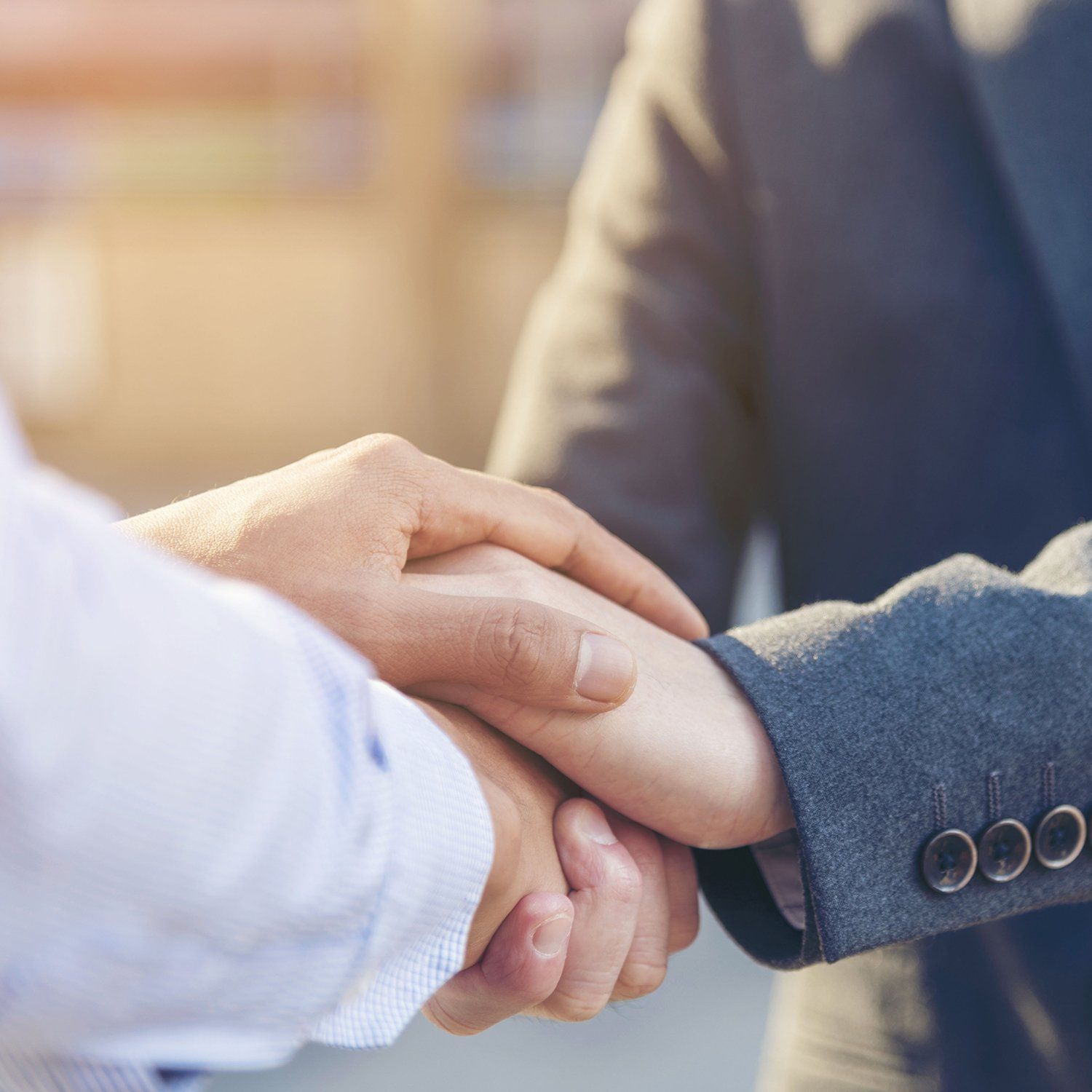 Two people shaking hands, likely a business agreement. Formal attire, outdoors.