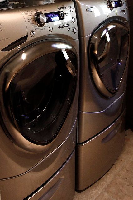 Two silver front-loading washing machines and dryers are stacked. They have curved glass doors and control panels.