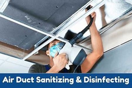 Person sanitizing air duct with a device, wearing a mask, in a building.