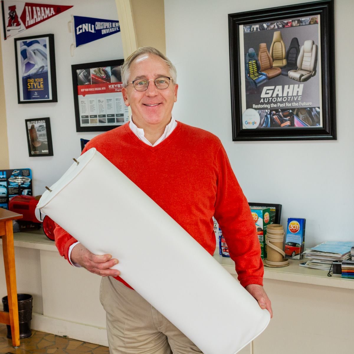 A man in a red sweater is holding a white tube in front of a gahh poster