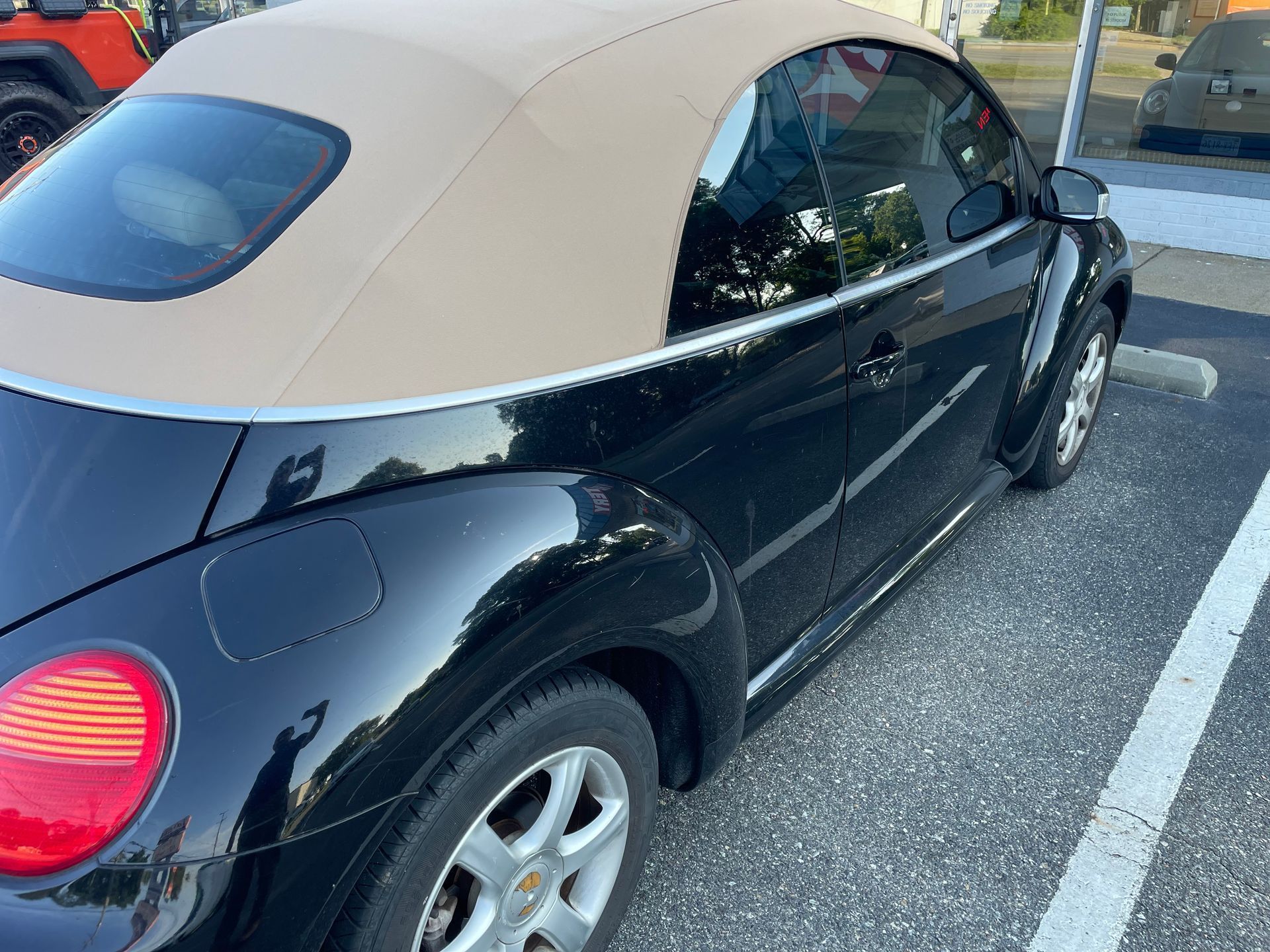 Black convertible Volkswagen Beetle with a tan top, parked on asphalt.