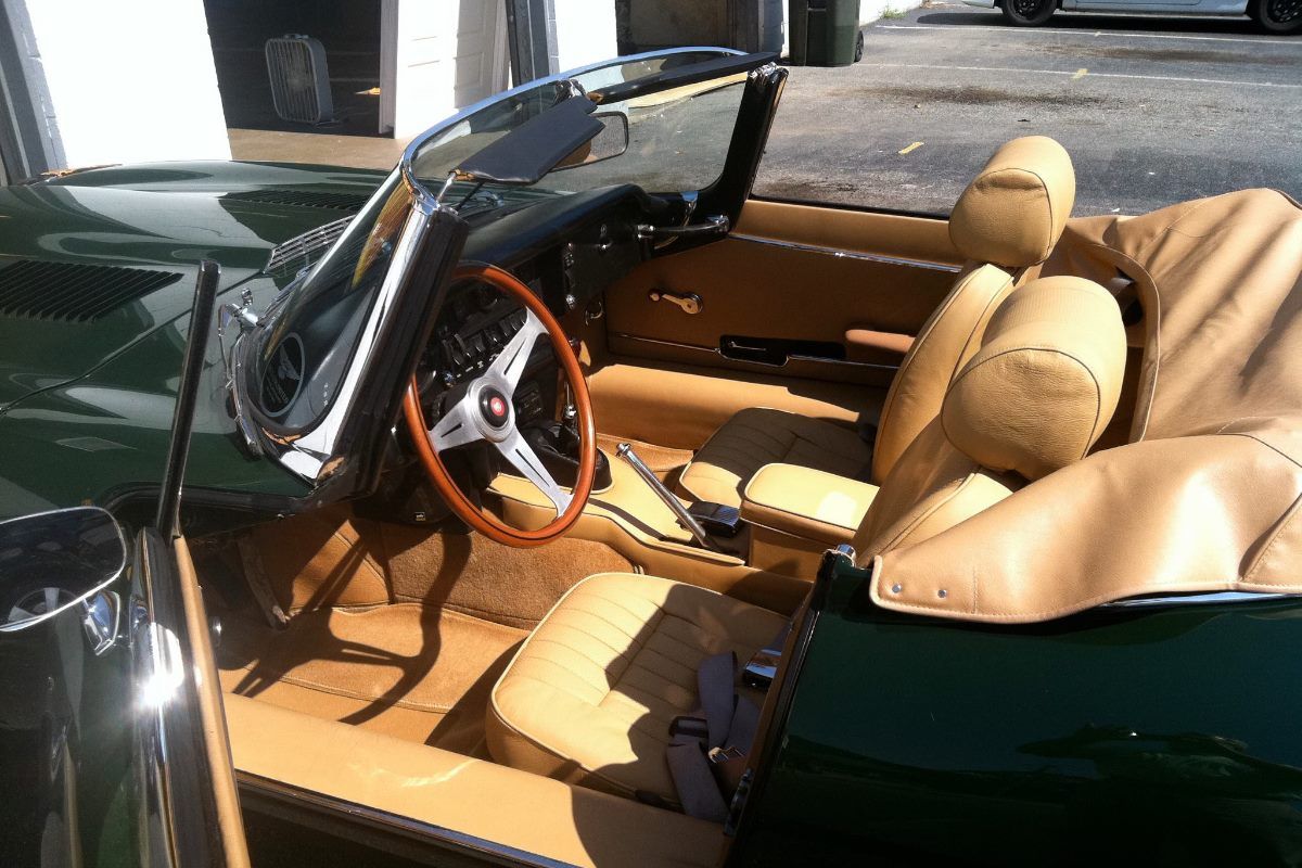The inside of a green convertible with tan seats and a wooden steering wheel