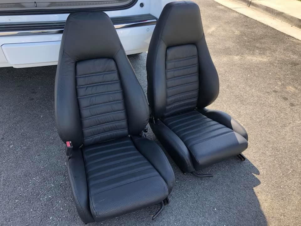 A pair of black leather seats are sitting in front of a white car.