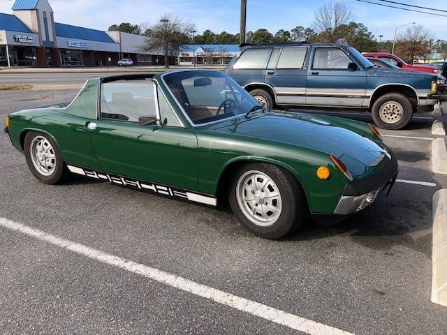 A green porsche is parked in a parking lot next to a blue suv.