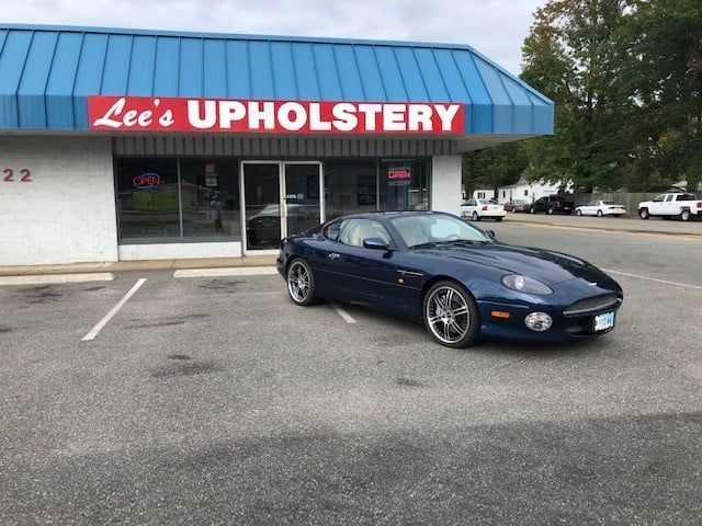 A blue sports car is parked in front of lee 's upholstery